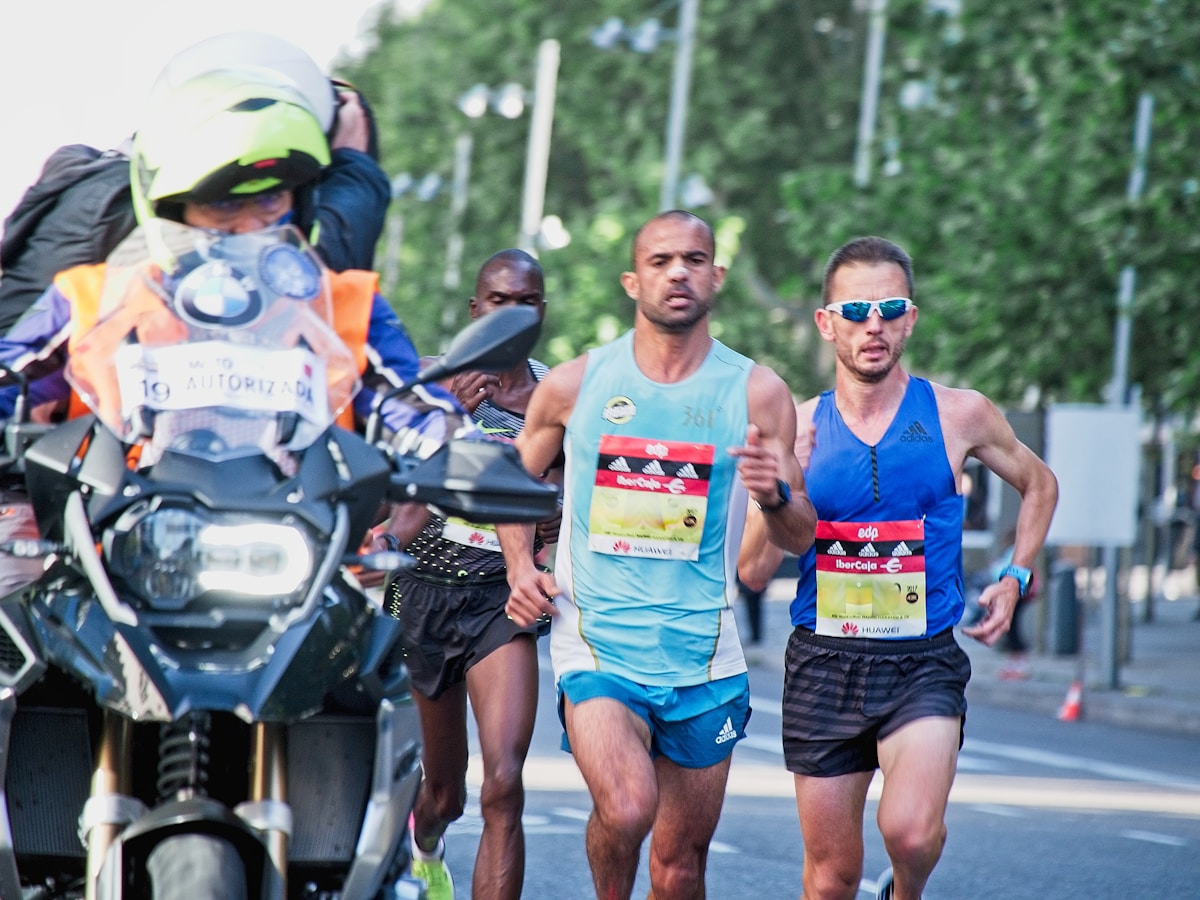 Coureurs de marathon en tenue sportive, escortés par un motard, dans un environnement urbain verdoyant.