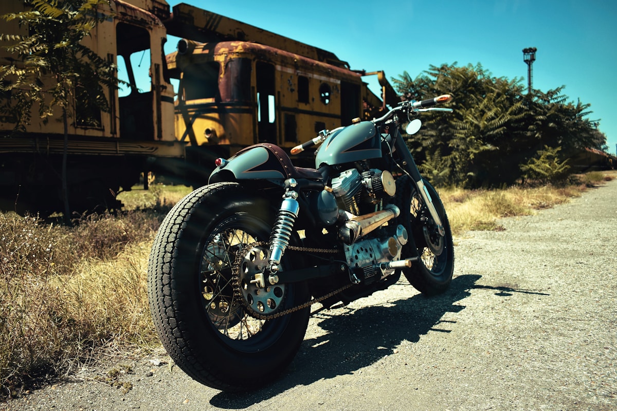 Moto vintage customisée, pneus larges, décor rustique en arrière-plan.