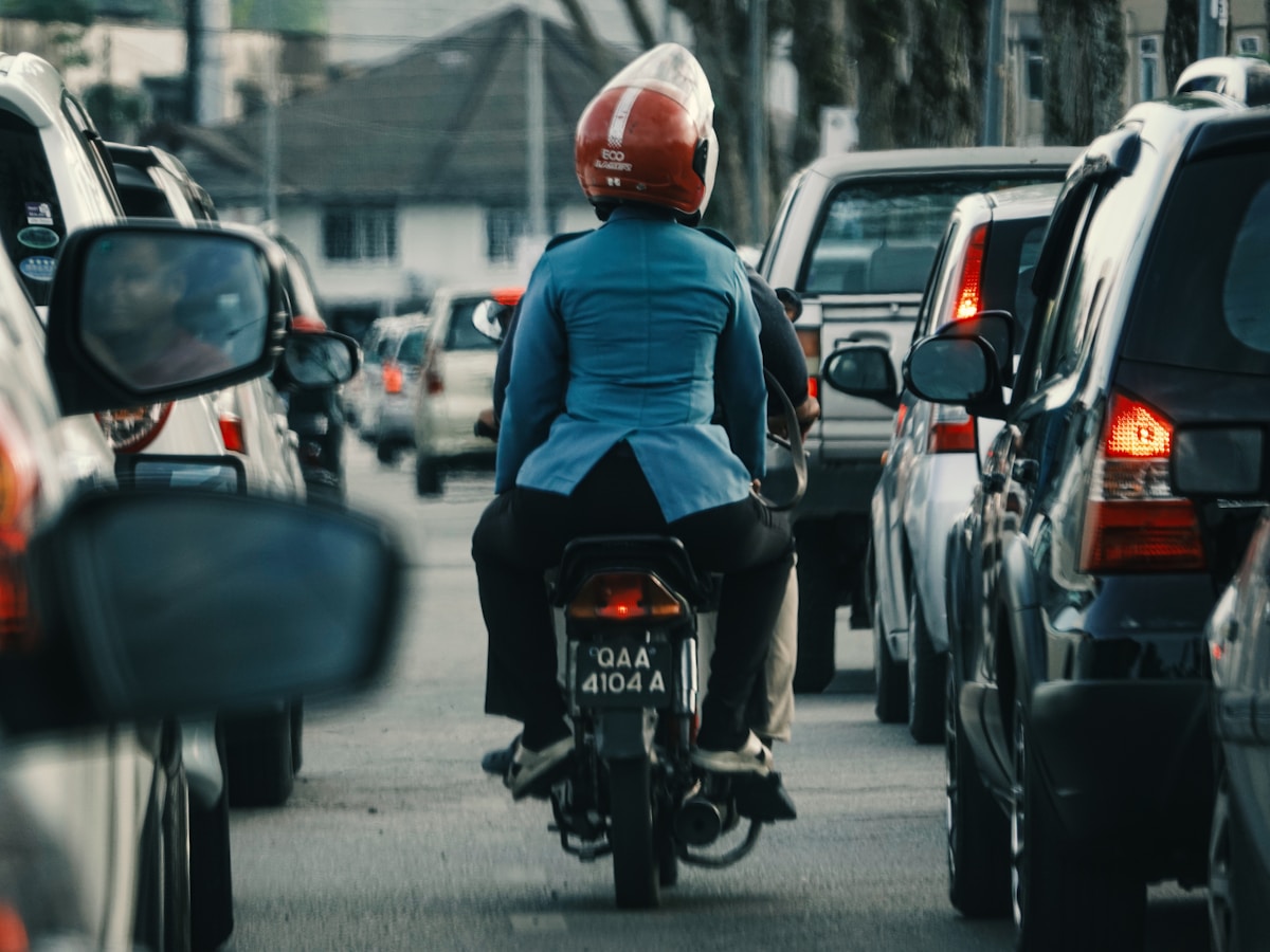 Motocycliste dans la circulation urbaine, casque rouge, vêtements bleus.
