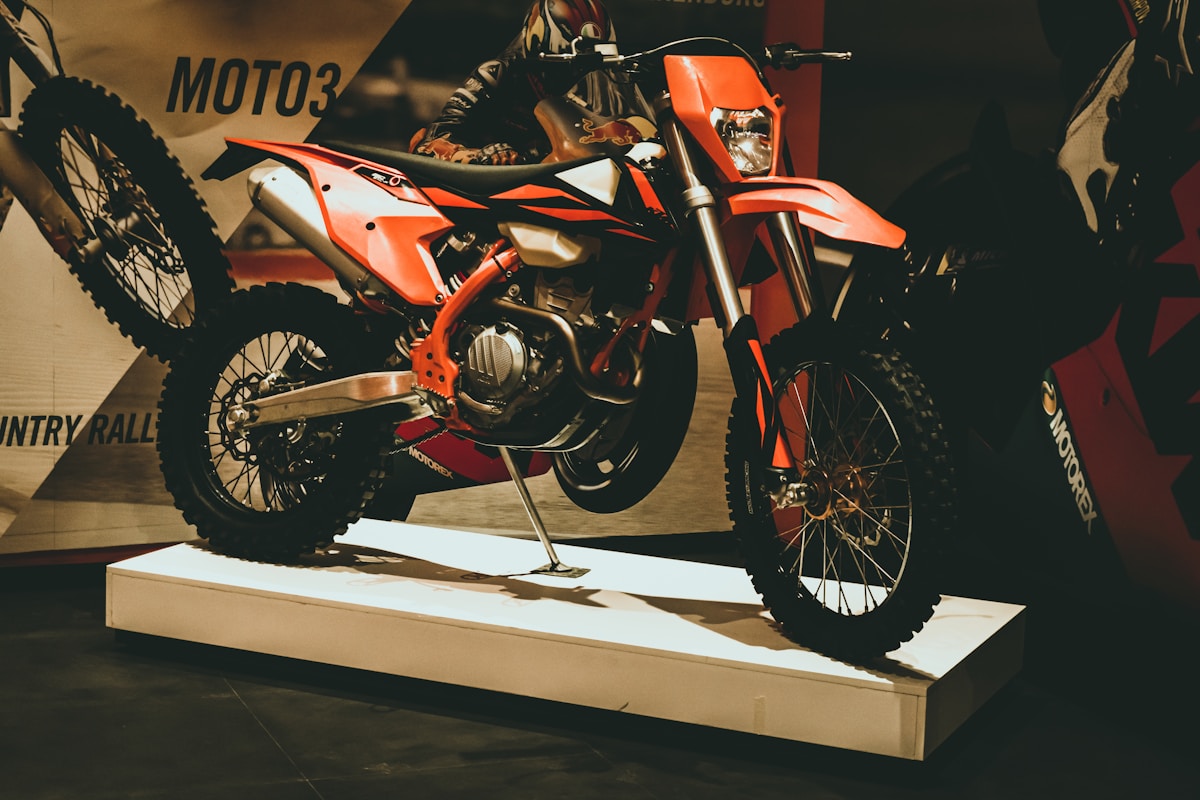 Moto tout-terrain orange vive sur un socle d'exposition.
