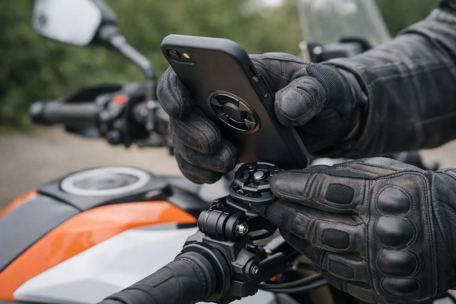 Gants de moto noirs, smartphone monté sur guidon, moto orange et noire.