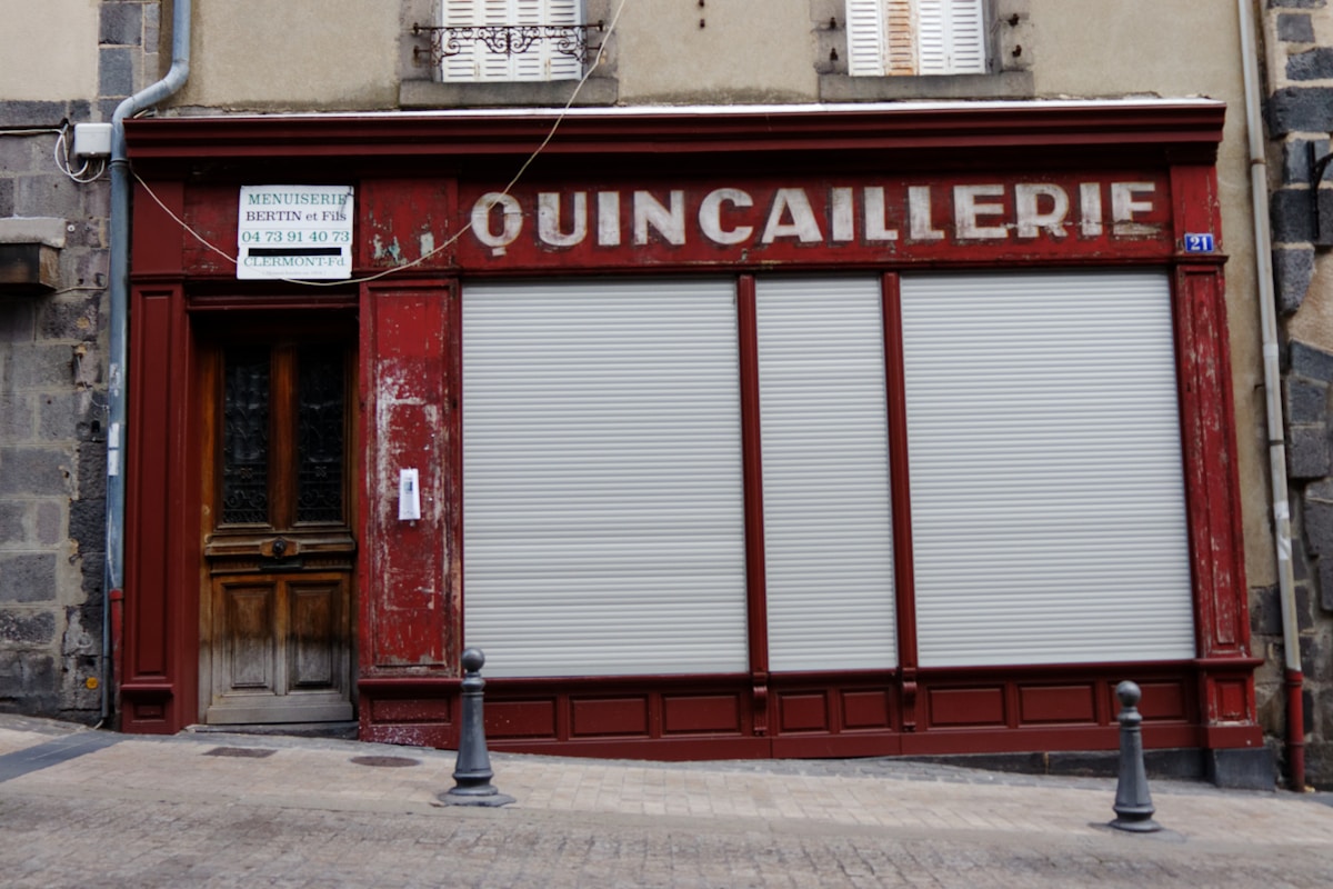 Quincaillerie, boutique fermée, façade rouge, volets blancs, devanture ancienne.