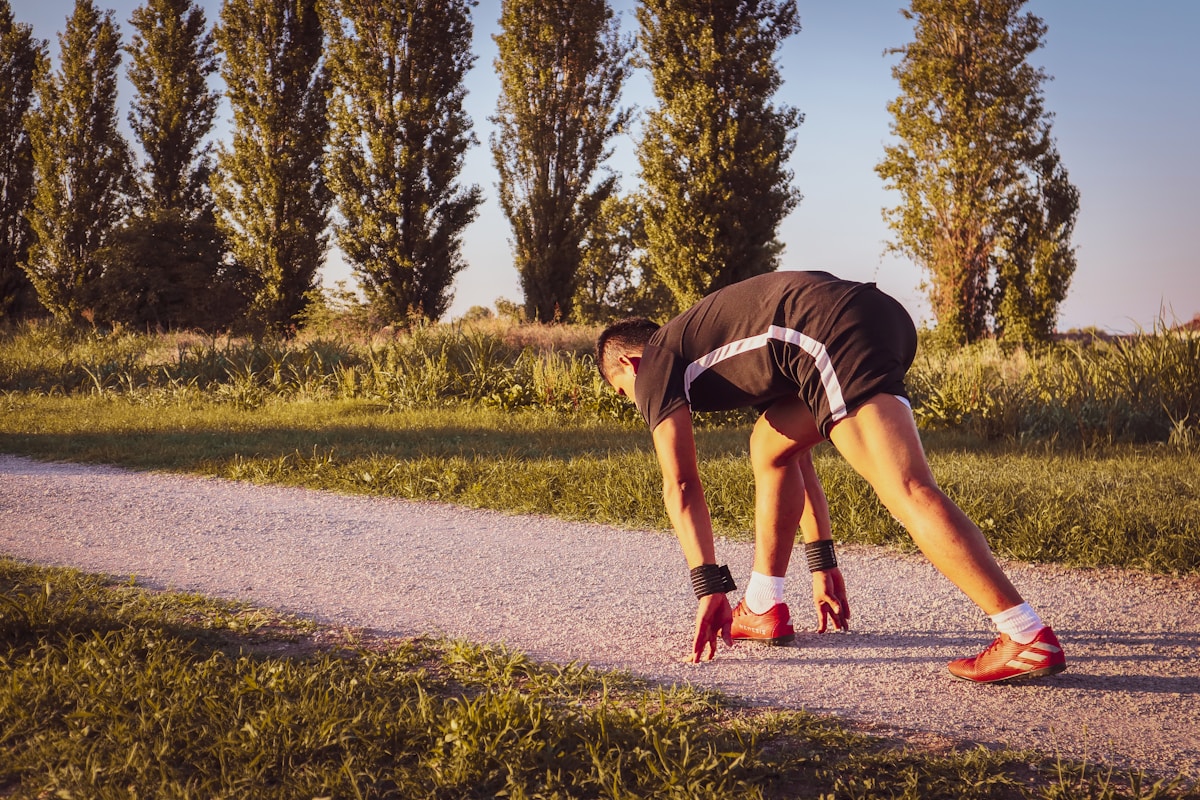 Coureur masculin en position de départ sur un chemin de campagne entouré d'arbres.
