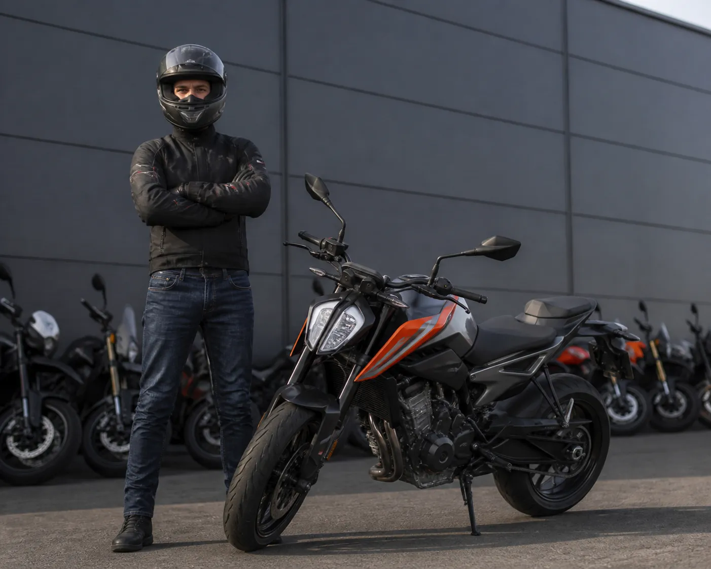 Motard en équipement de sécurité posant à côté d'une moto noire et orange.