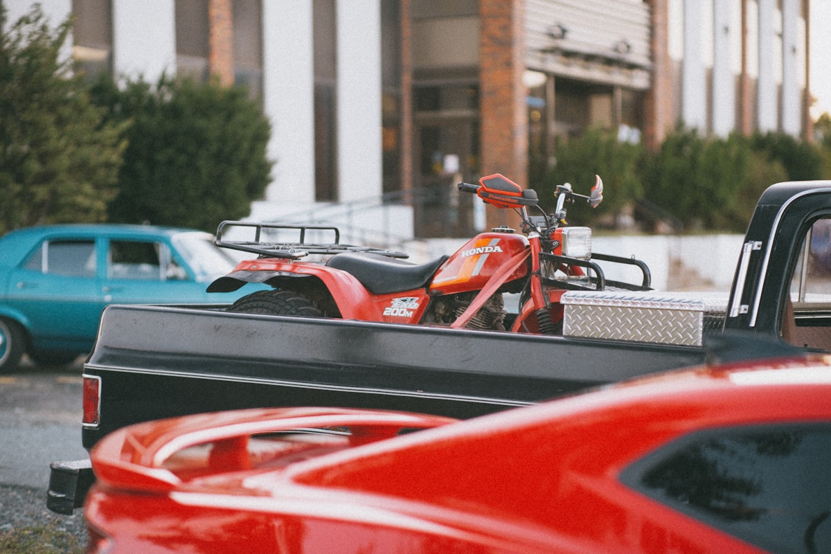 Camionnette rouge transportant un quad Honda orange sur un plateau.