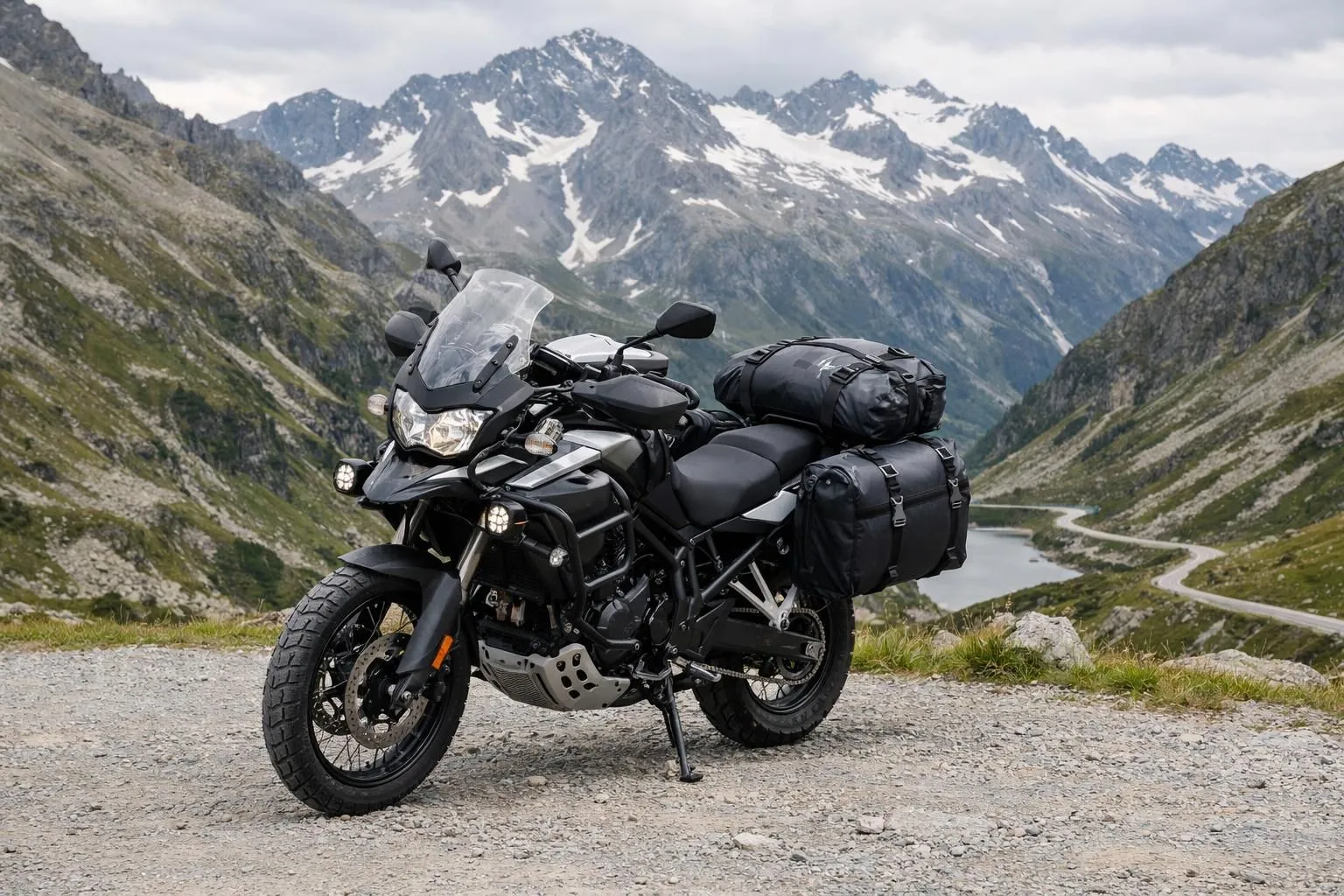 Accessoires essentiels de moto de tourisme montés sur un trail : sacoches étanches, sacoche de réservoir avec porte-carte, barres de protection et phares LED, garée sur un col alpin suisse avec paysage alpin.