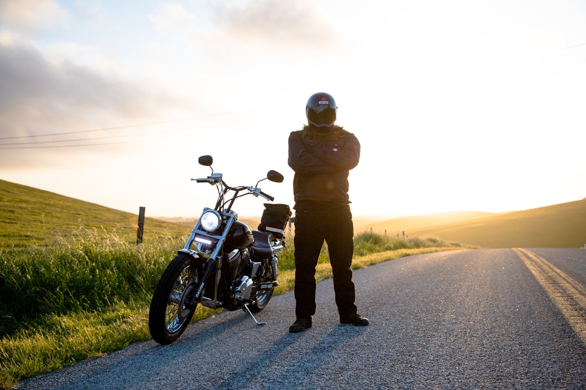 Motard en tenue de protection sur une route de campagne au coucher de soleil.