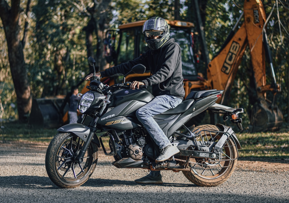 Motocycliste en équipement de sécurité sur une moto noire dans un environnement forestier.