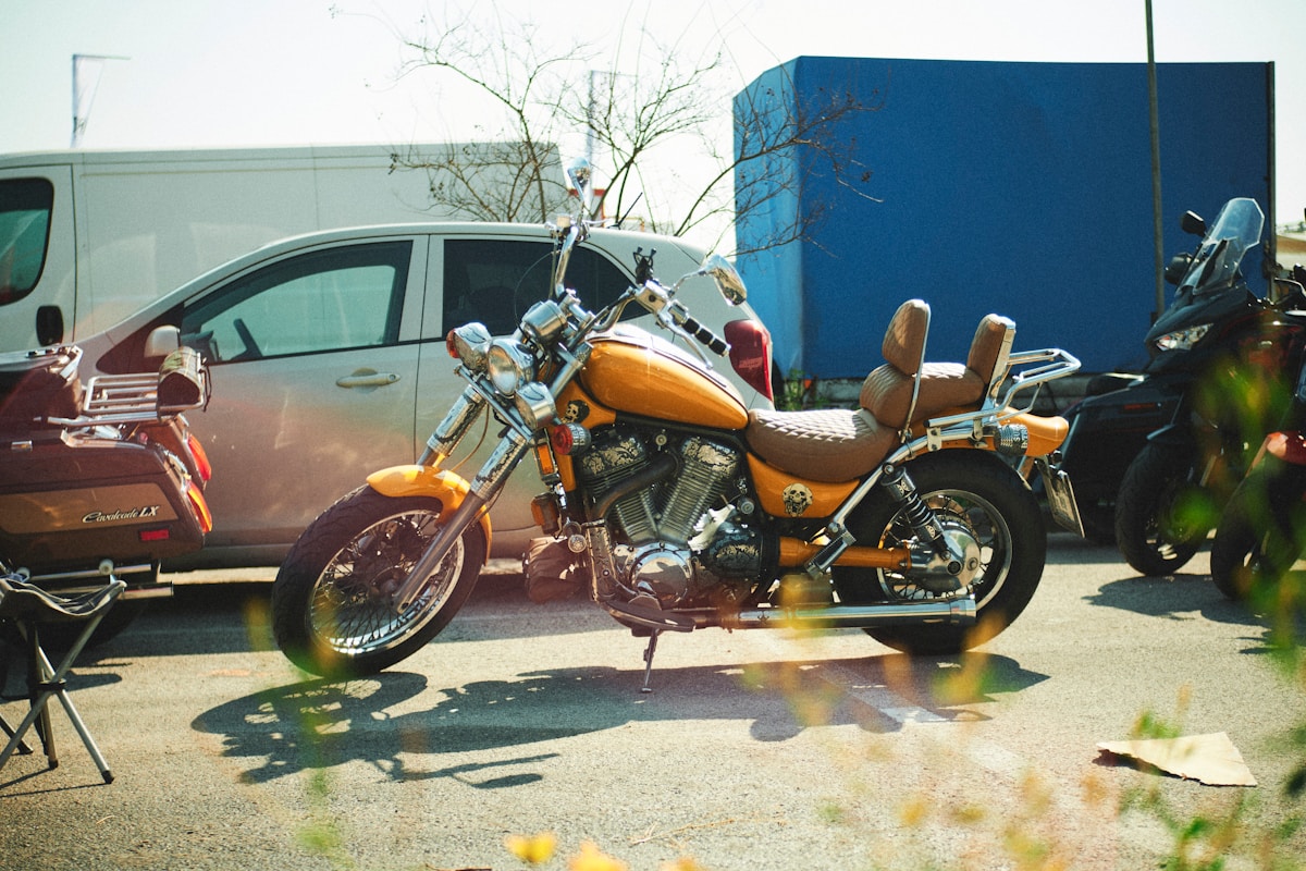 Moto orange garée devant un bâtiment bleu, avec des branches d'arbres en arrière-plan.