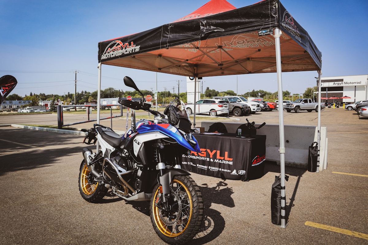 Moto tout-terrain bleue et blanche avec tente d'exposition dans un parking.