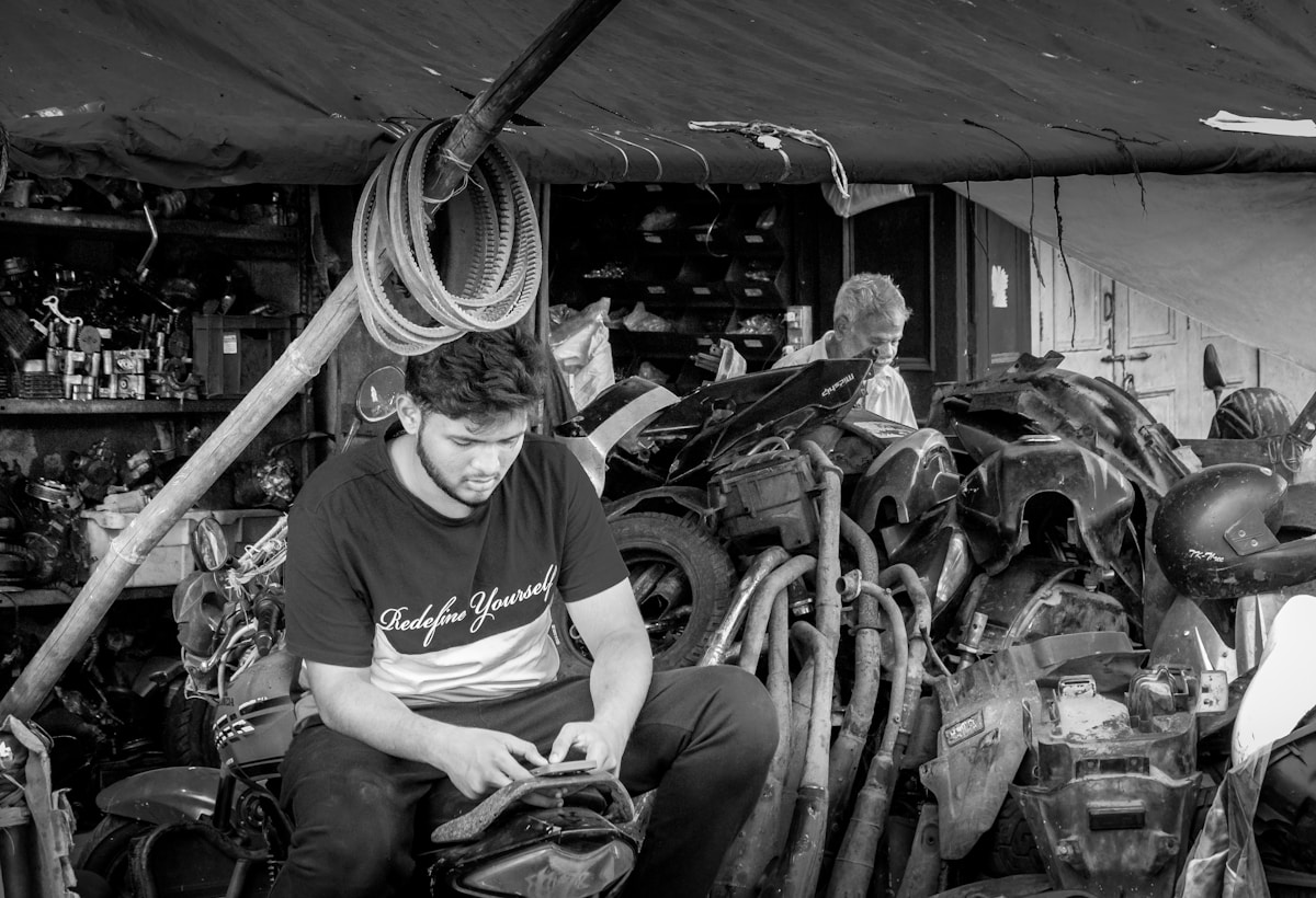 Homme dans un atelier de réparation de motos, entouré d'outils et de pièces détachées.