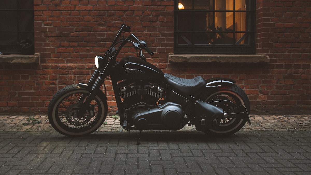 Moto noire customisée garée devant un mur de briques.