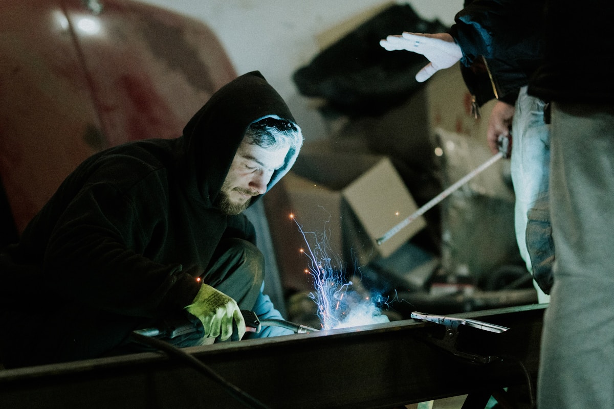 Homme soudant dans un atelier sombre et industriel.