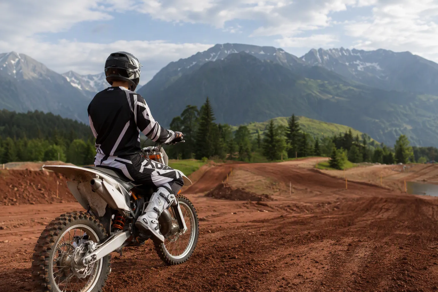 Moto motocross 125 cc sur piste suisse, pilote en casque, montagne en arrière-plan.