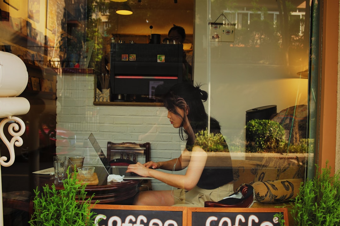 A small business owner works on their laptop in a cozy, sunlit cafe, looking focused and creative.