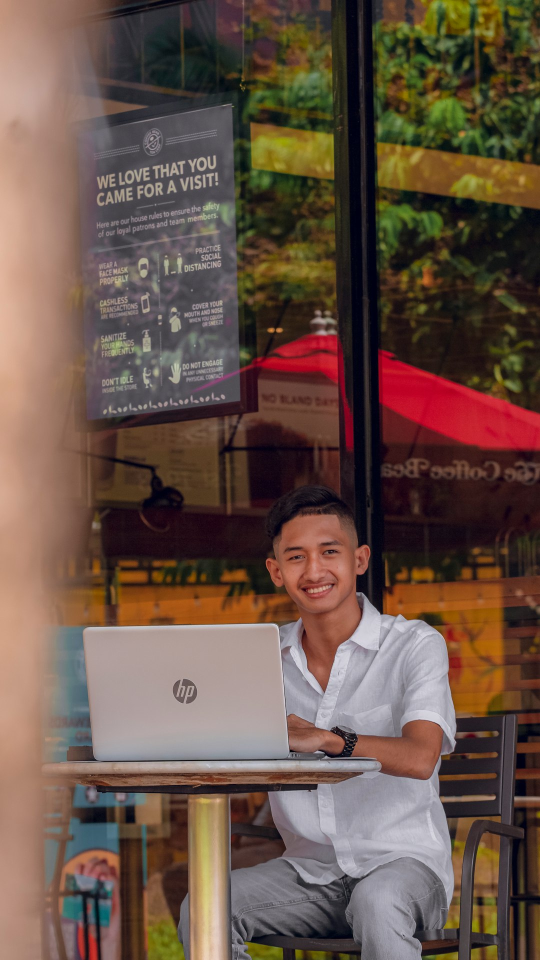 A cheerful small business owner working on a laptop in a bright, modern cafe. They are smiling, looking confident and in control of their work.
