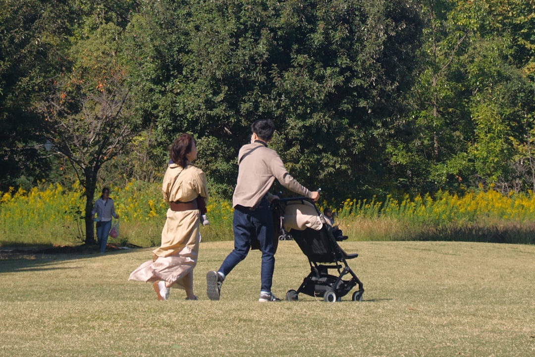 Une famille rie aux éclats en se promenant dans un parc verdoyant, tenant les mains de leurs deux jeunes enfants. Photo par Vitolda Klein sur Unsplash.