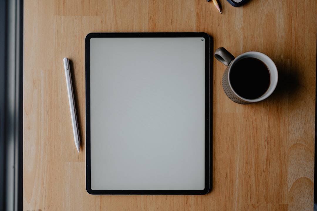 A close-up shot of a person sketching website layout ideas in a notebook on a wooden desk, with a laptop and coffee nearby.