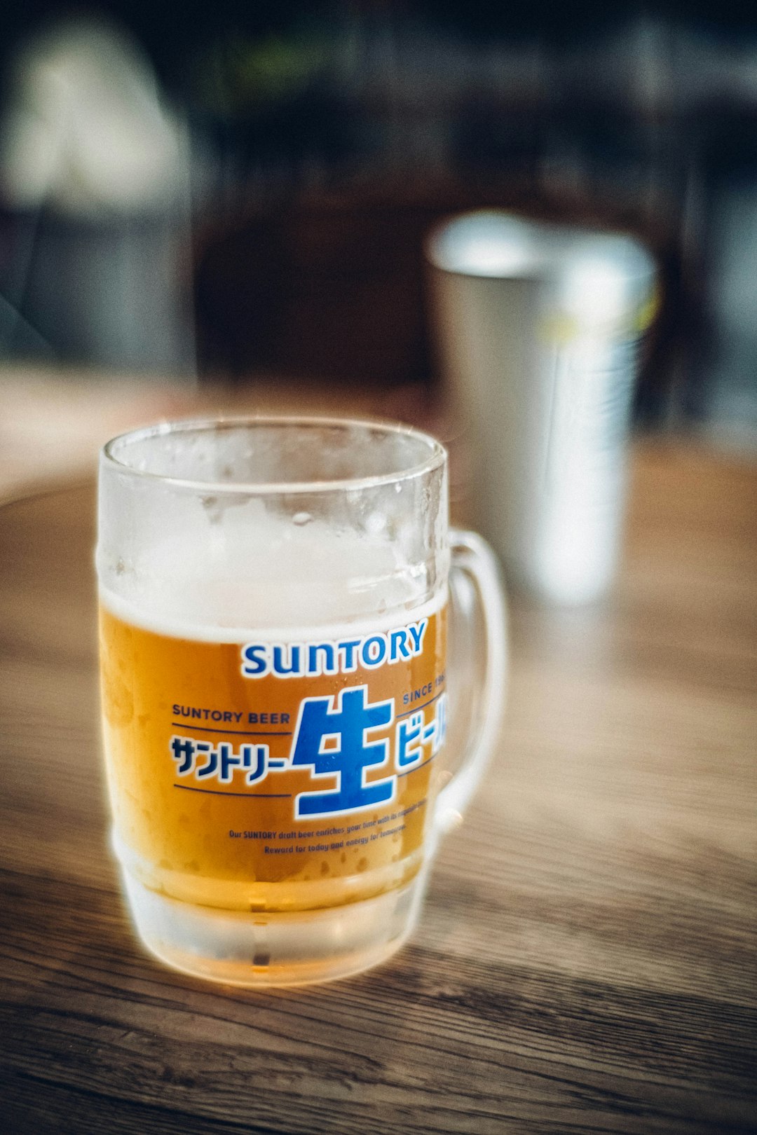 A close-up of a frothy draft beer in a glass on a wooden bar counter, with the blurred background of a pub.