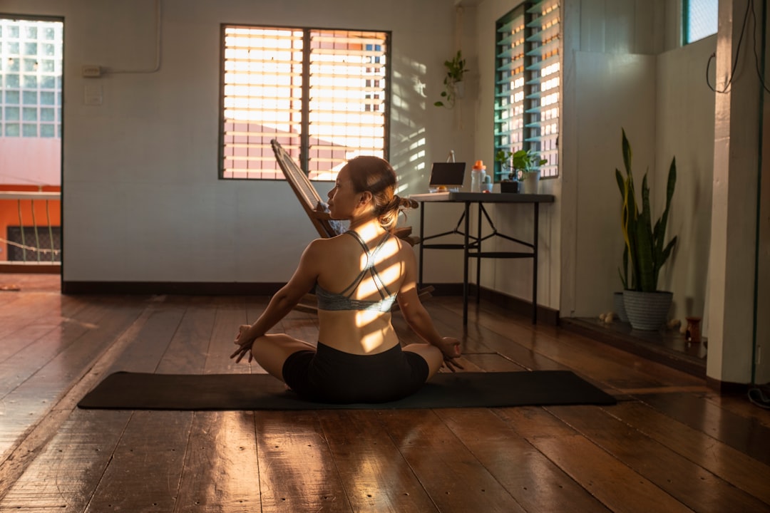 Une femme pratique la méditation assise en tailleur sur un tapis de yoga dans un salon lumineux et apaisant.