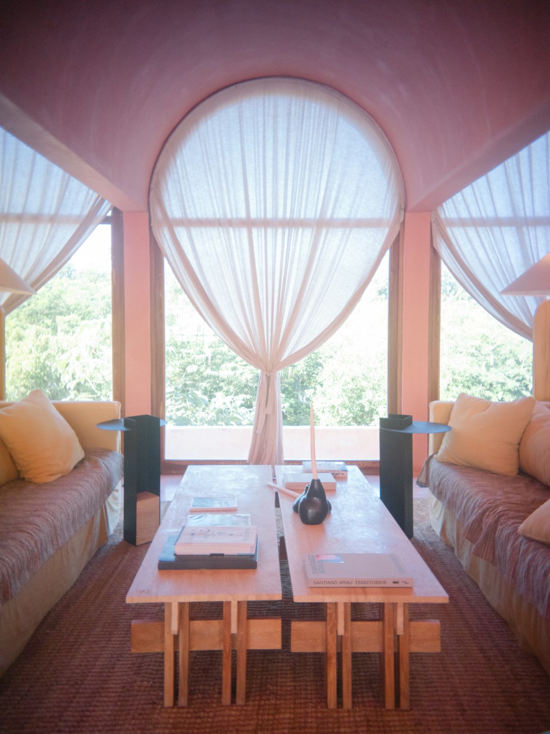 Un salon lumineux et confortable avec de grandes fenêtres ouvertes donnant sur un jardin verdoyant, les moustiquaires étant à peine visibles.