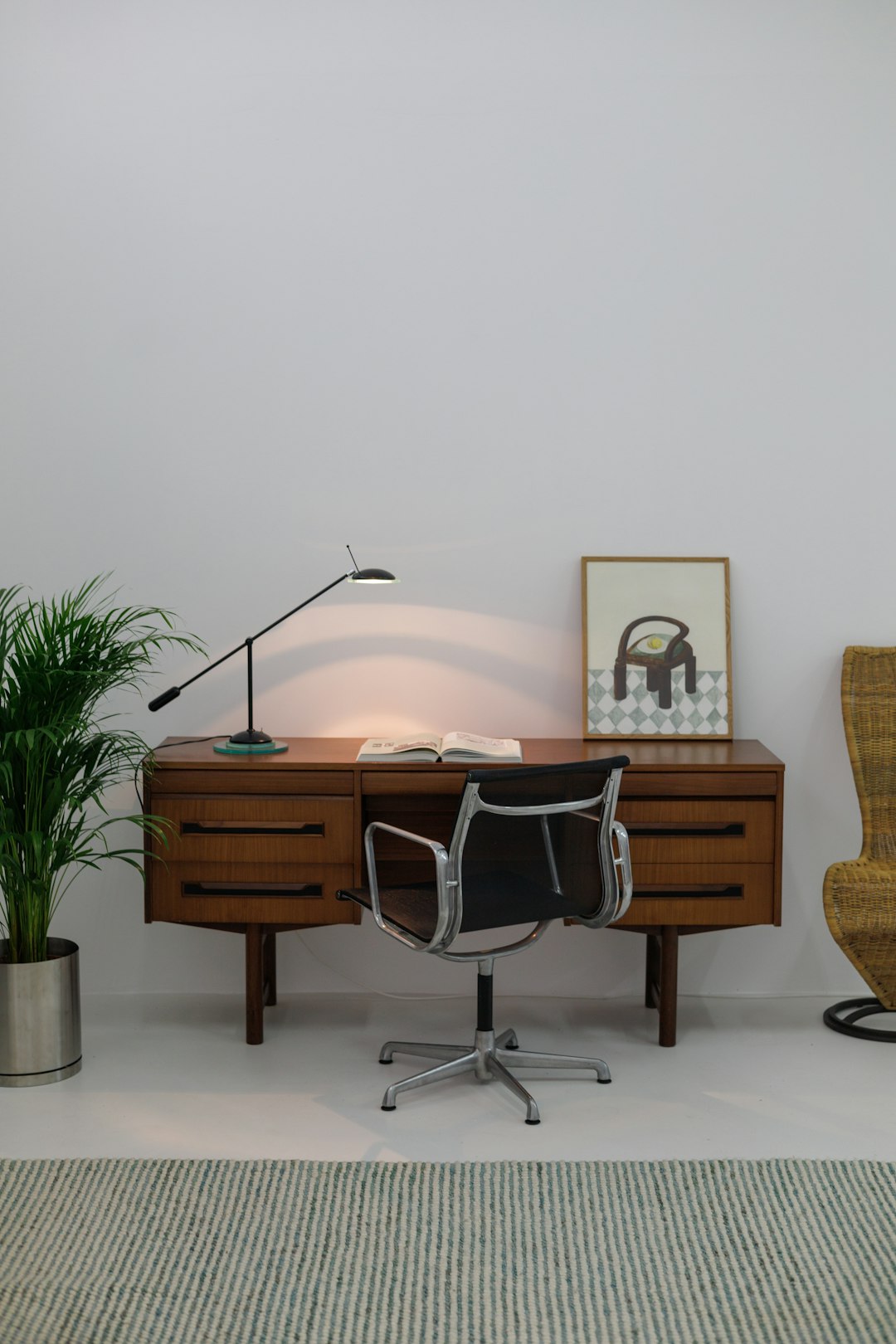 Un bureau de style milieu du siècle en bois sombre placé devant une fenêtre avec une chaise en cuir assortie, évoquant une ambiance vintage et design.
