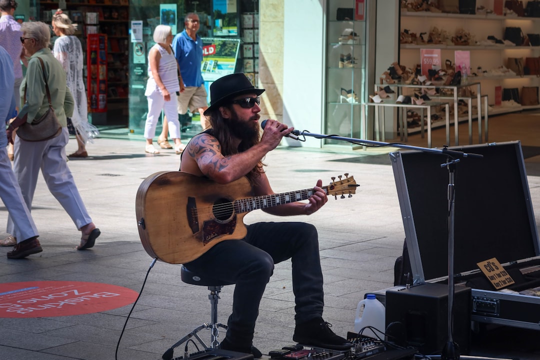 A street musician with a guitar smiles warmly as an audience member in the foreground holds up their smartphone to scan a QR code displayed on a small sign.