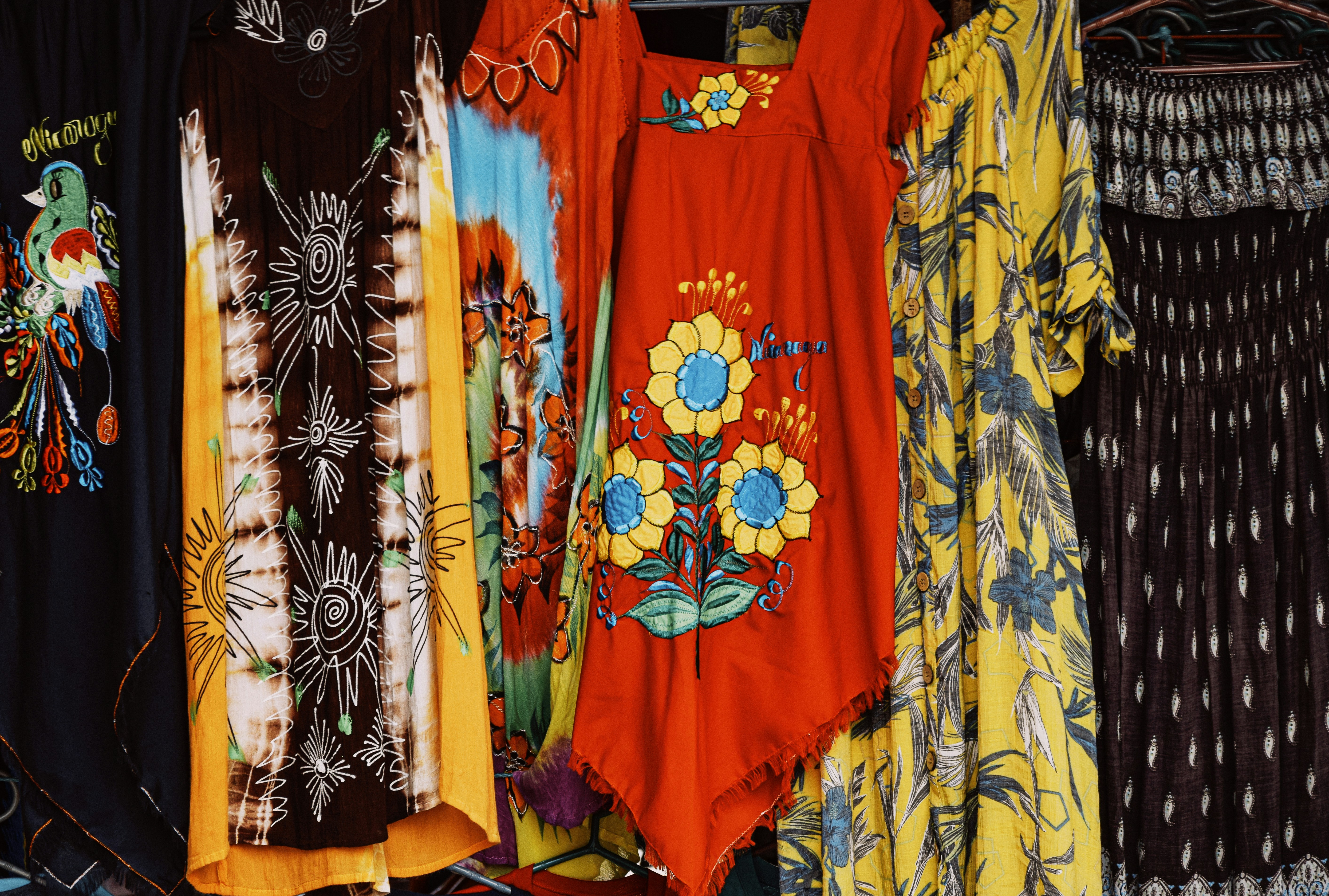 Une variété de robes de style californien, aux couleurs et motifs vifs, suspendues sur un portant.