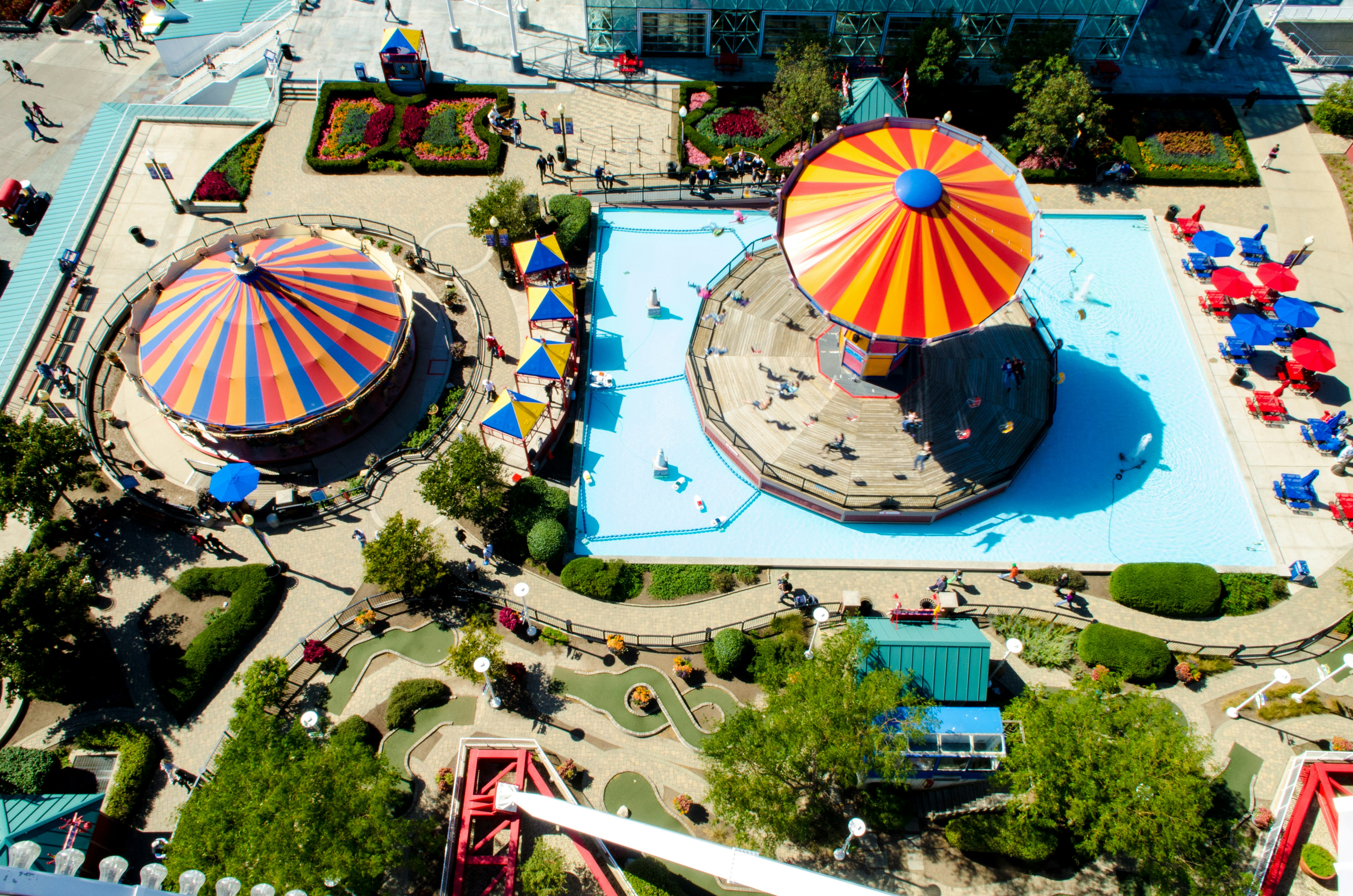 Vue aérienne d'une piscine extérieure ensoleillée, bondée de monde, avec des parasols colorés.