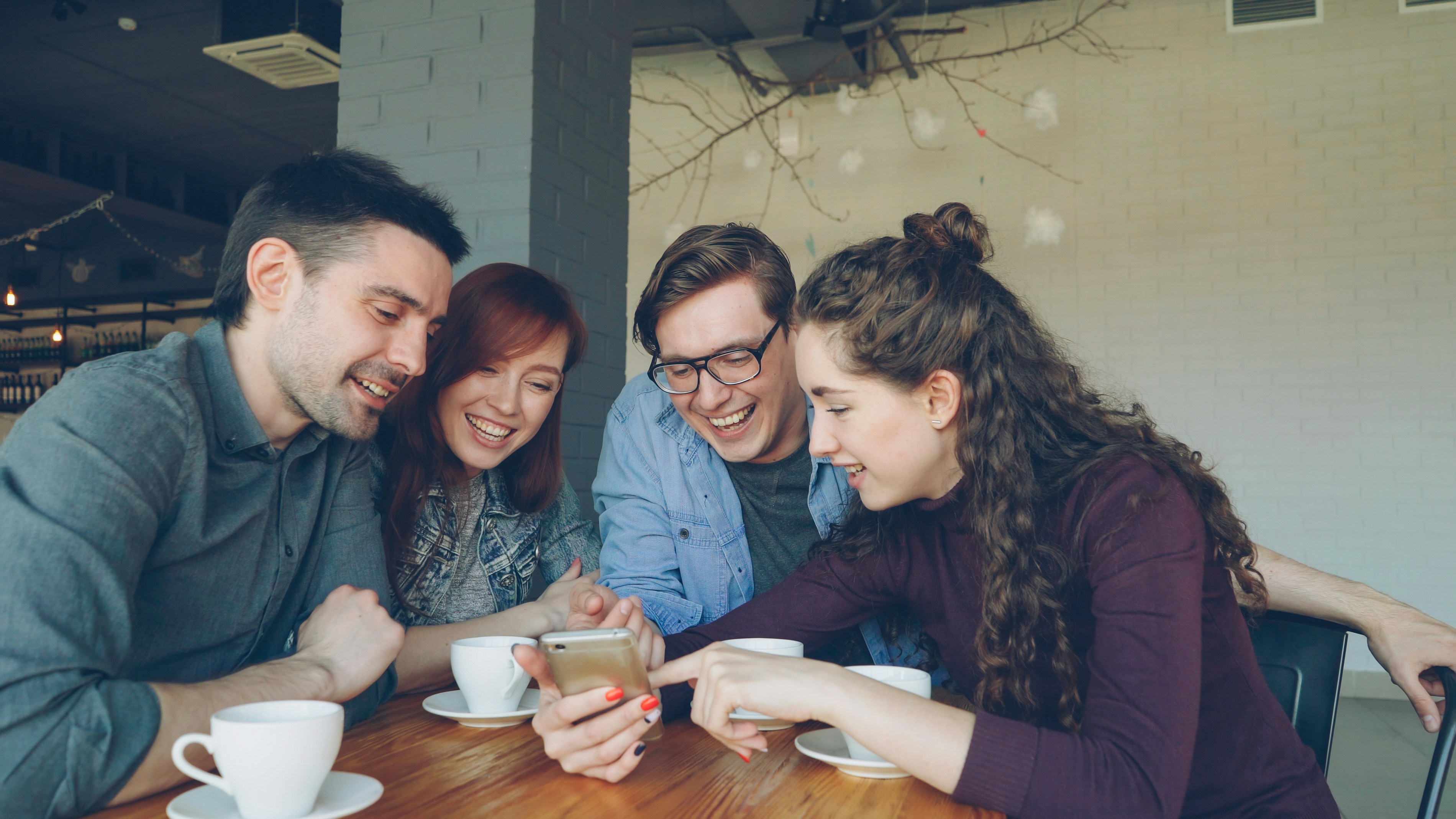 Un groupe d'amis riant ensemble dans un café, des tasses de café et des verres de maté glacé sur la table, symbolisant la convivialité.