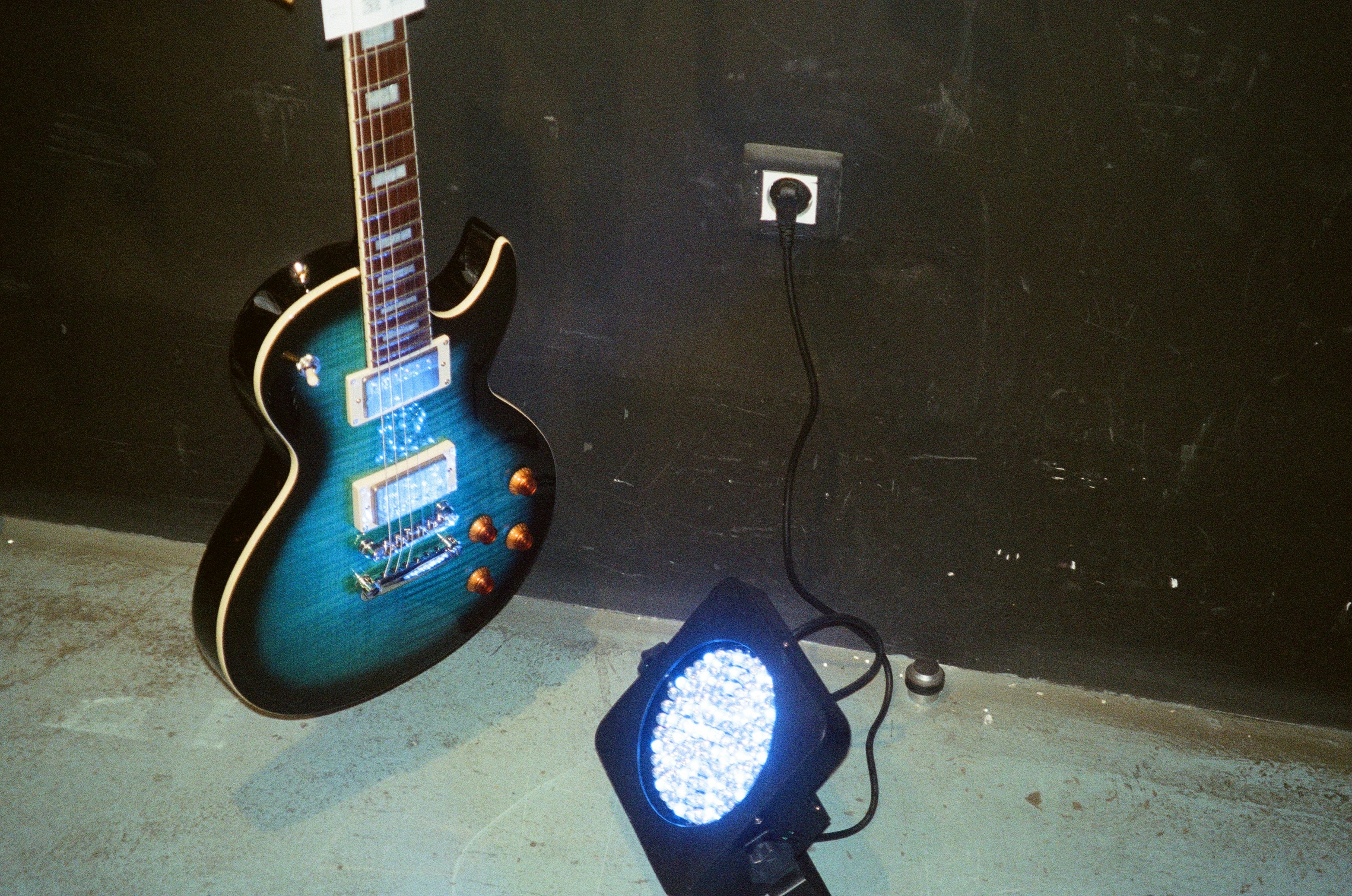 Gros plan sur une guitare électrique posée sur un stand sur une scène faiblement éclairée, prête pour un concert.