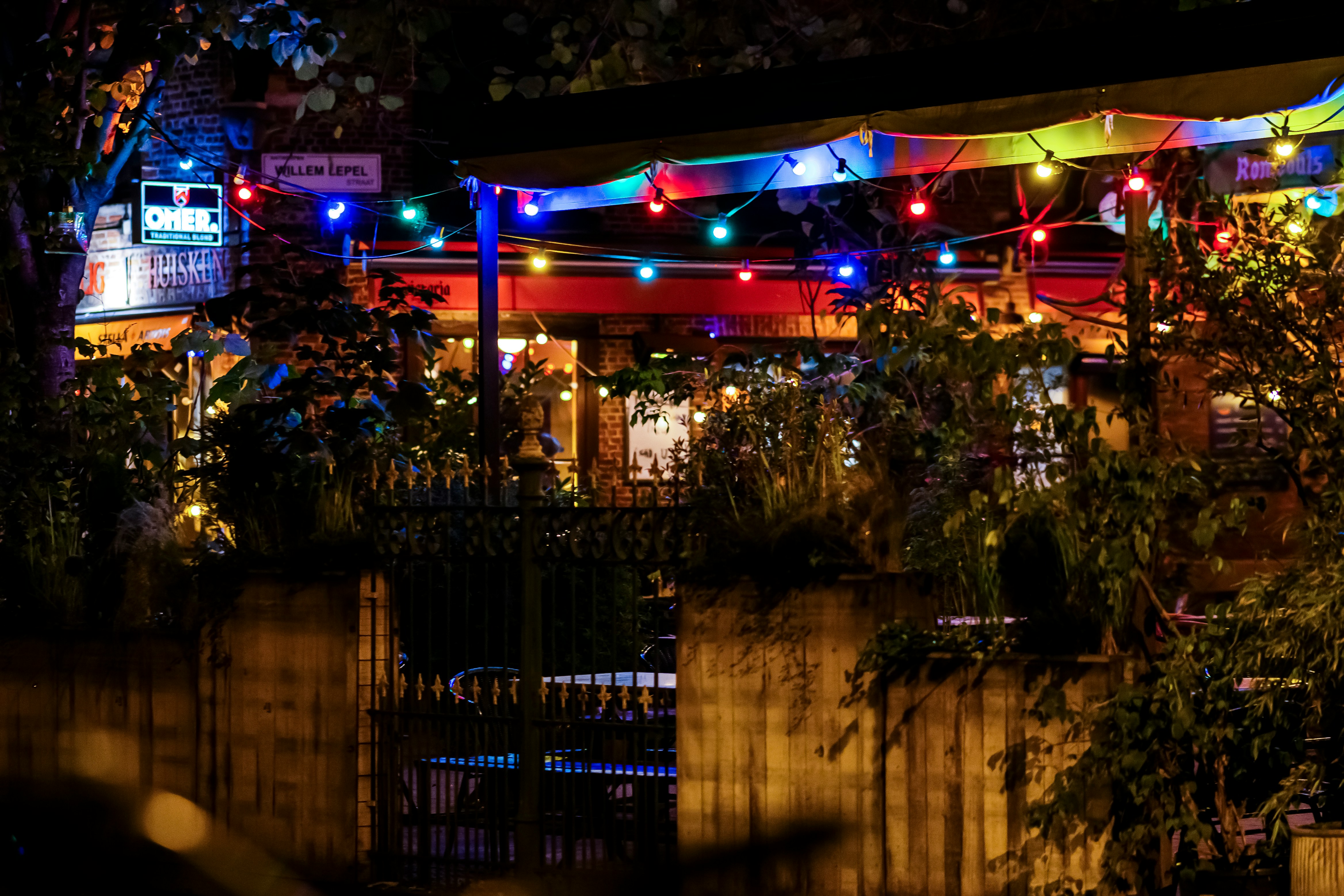 Vue d'une terrasse de pub en soirée d'été, avec des guirlandes lumineuses et des gens attablés, buvant et discutant joyeusement.