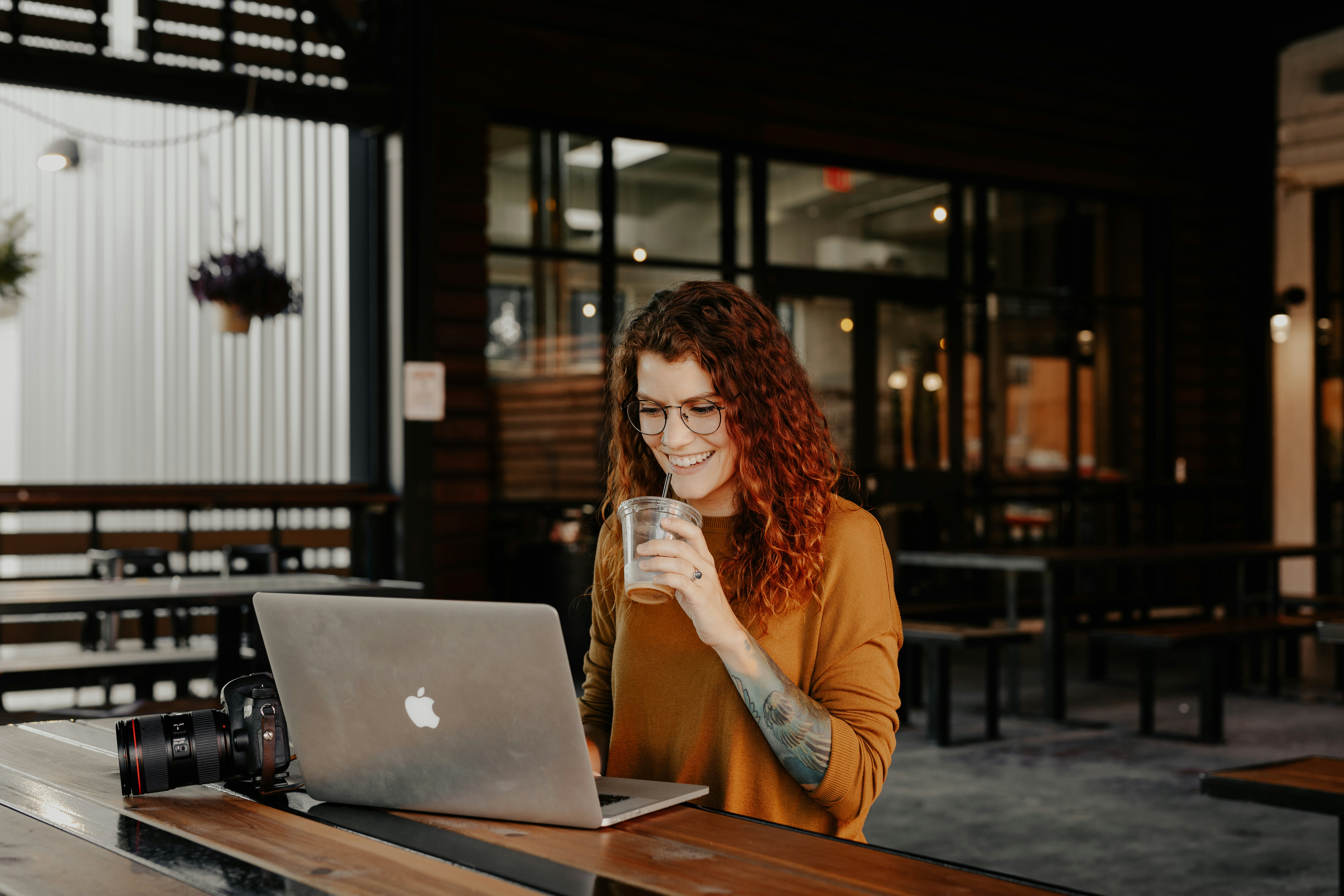 Someone smiling while working on a laptop in a bright coffee shop, showing just how easy and accessible modern tools have become.