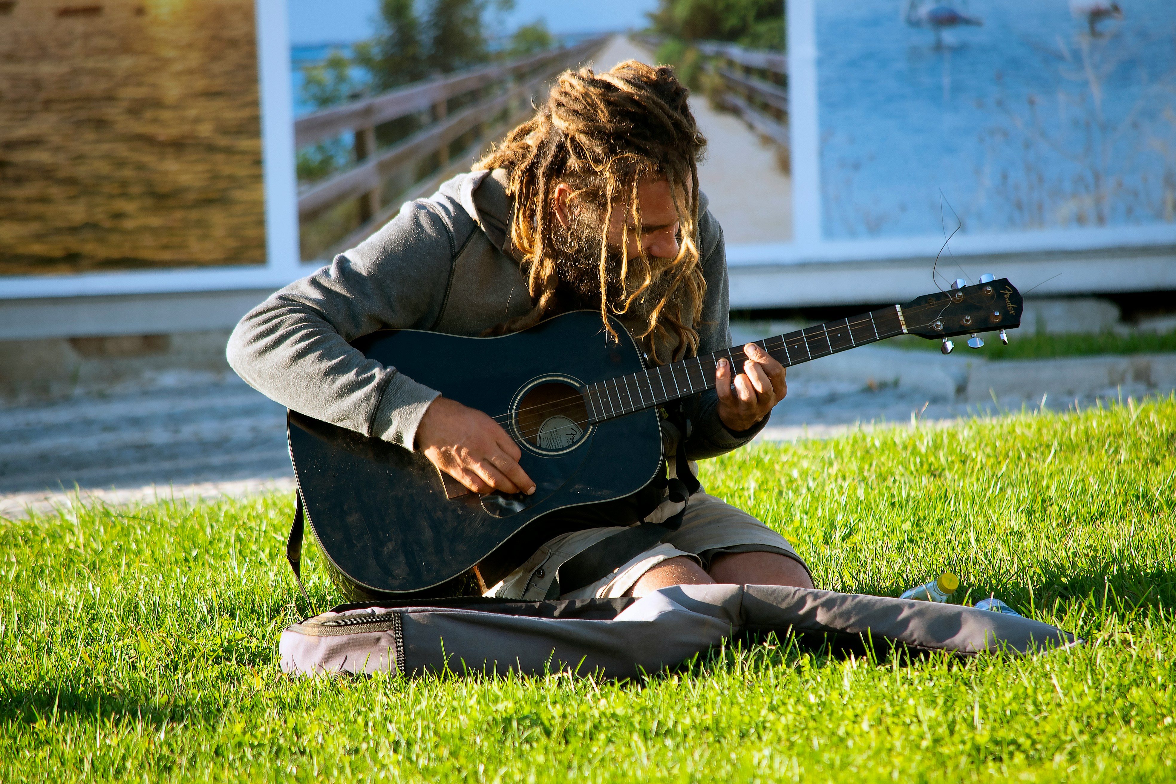 A musician sits thoughtfully on a stool in a dimly lit room, tuning their acoustic guitar as they get ready for a performance.