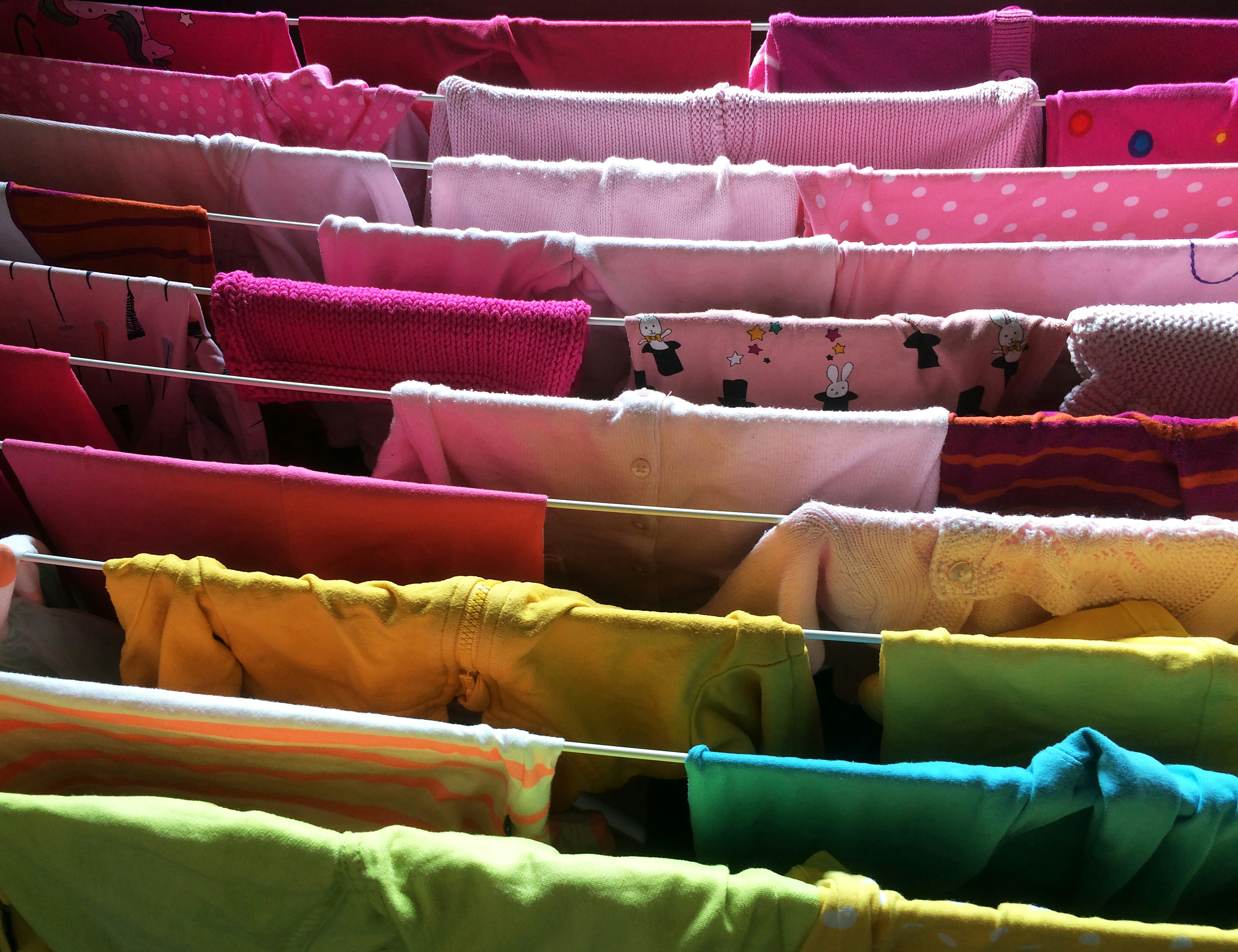 Des étagères de rangement bien éclairées contenant des piles de pulls et de t-shirts soigneusement pliés, organisés par couleur.