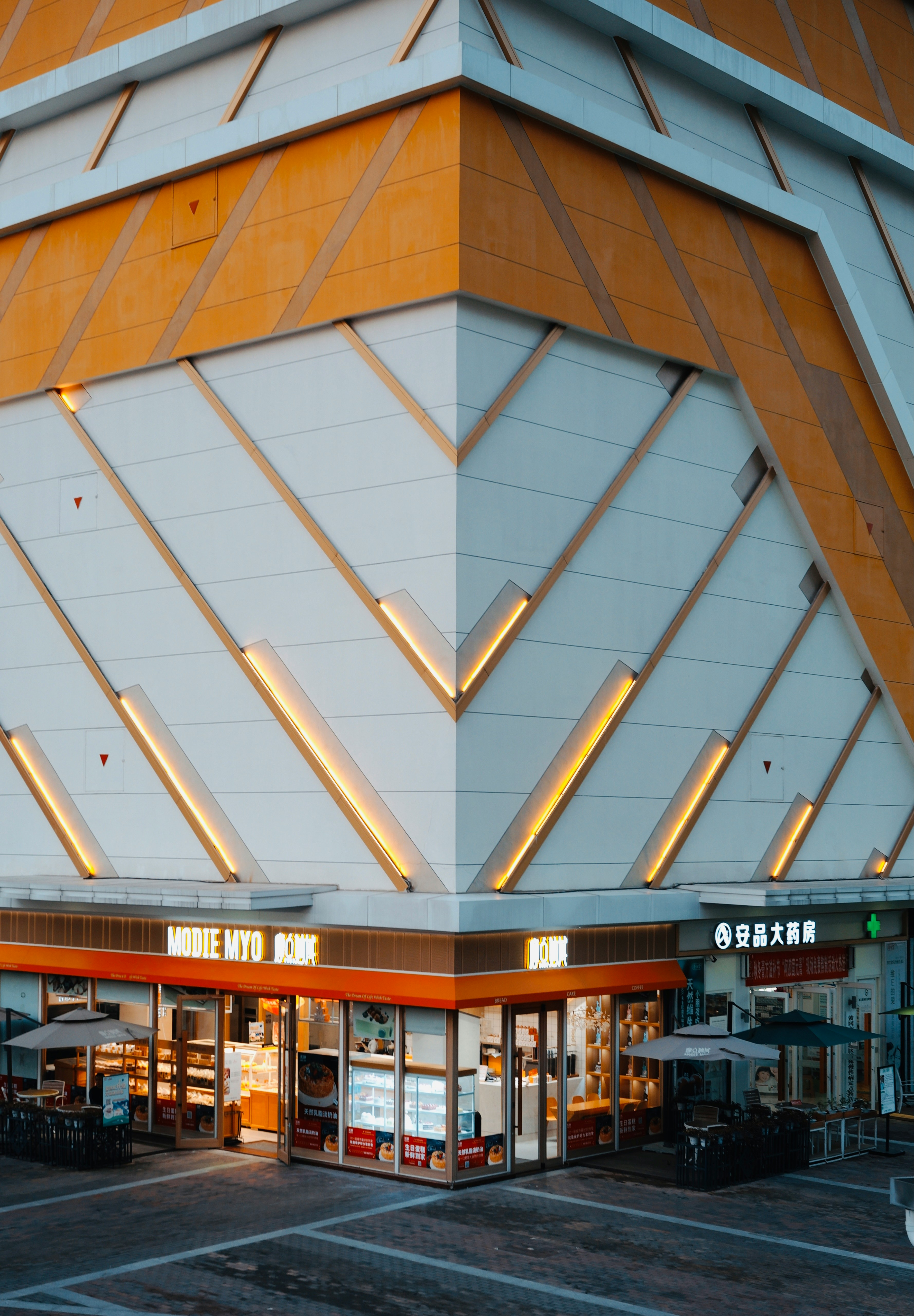 Une personne tenant une télécommande blanche et moderne, pointée vers une fenêtre où des stores motorisés sont en train de se fermer.