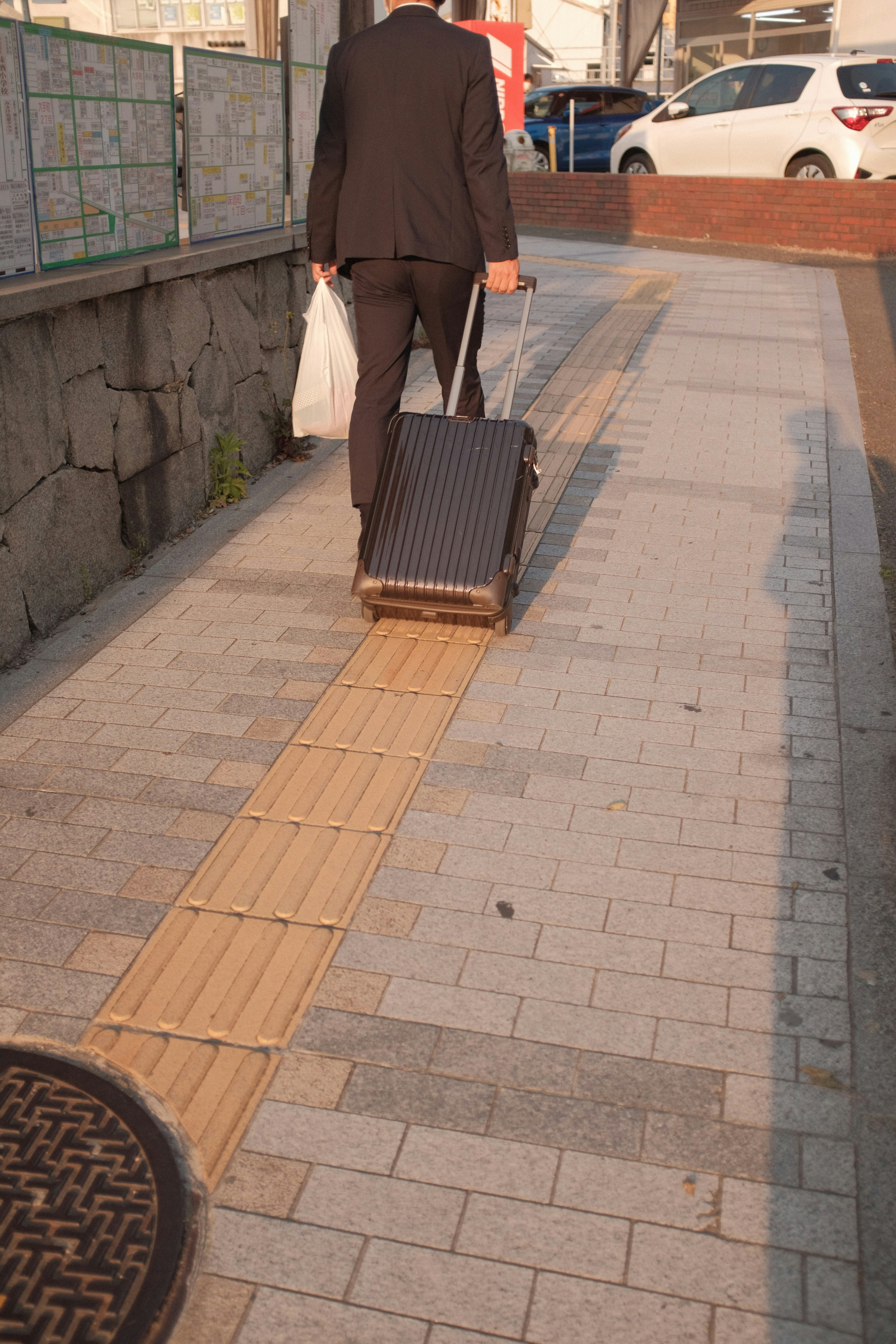 A performer is seen from behind packing up their gear on a city sidewalk as the sun sets, symbolizing the end of a day's work.