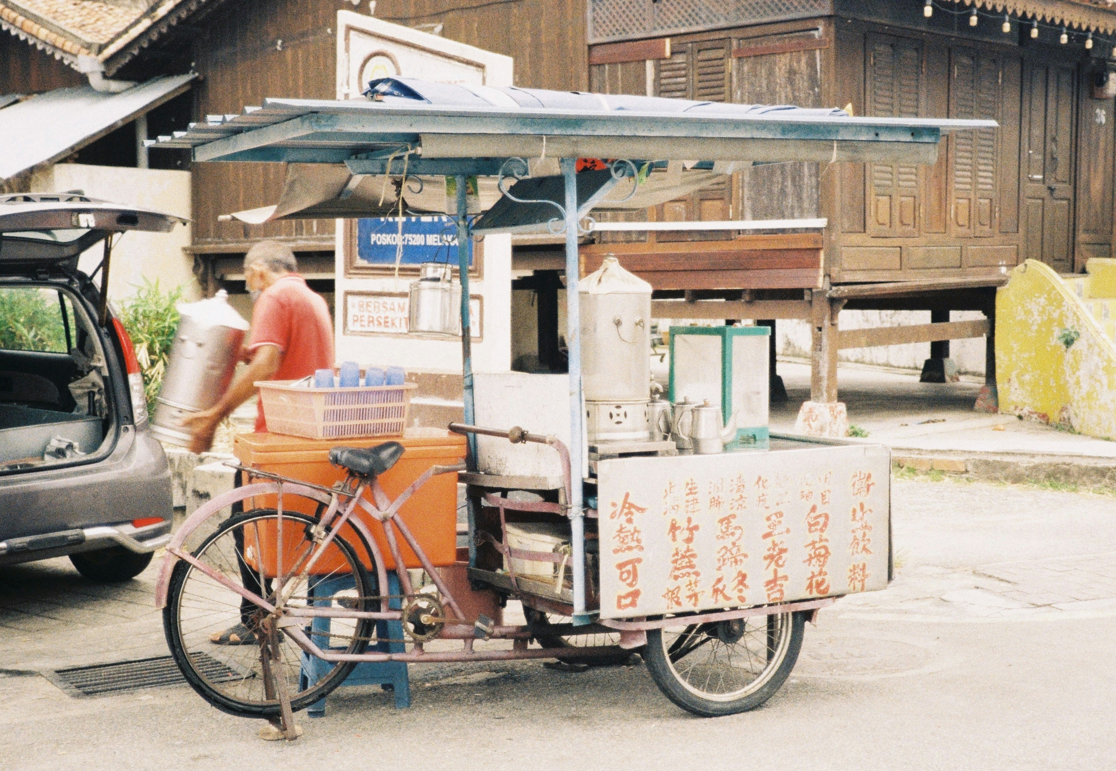 Un livreur souriant sur un vélo-cargo passe un carton de produits locaux à la propriétaire d'une petite épicerie devant sa boutique.