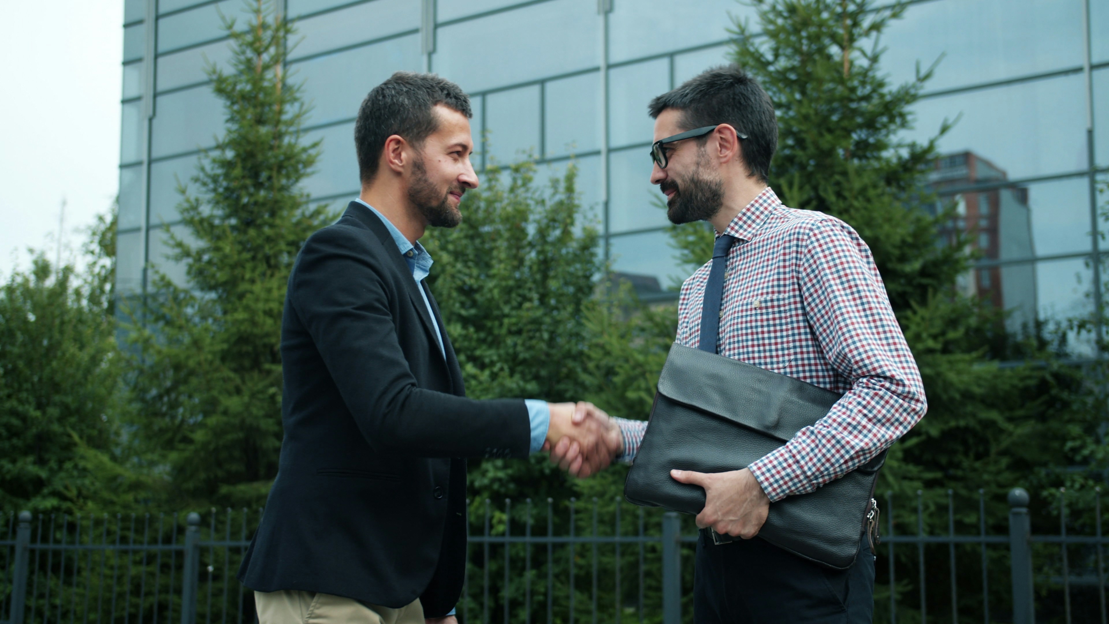 Une poignée de main entre deux professionnels devant un bâtiment moderne, symbolisant le partenariat stratégique entre une PME et sa fiduciaire.