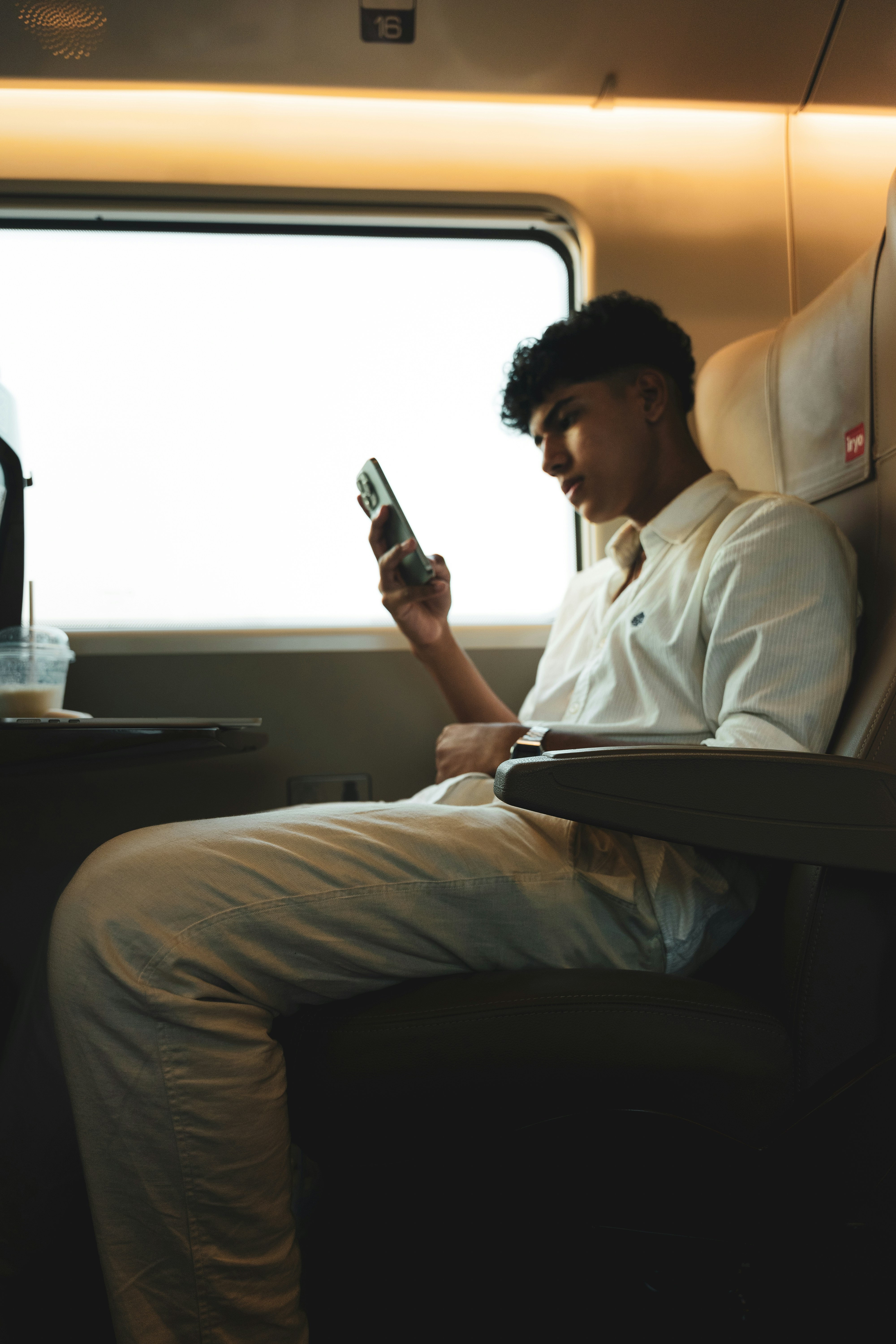 Un jeune professionnel assis dans un train regarde son smartphone avec concentration, des écouteurs aux oreilles, optimisant son temps de trajet.