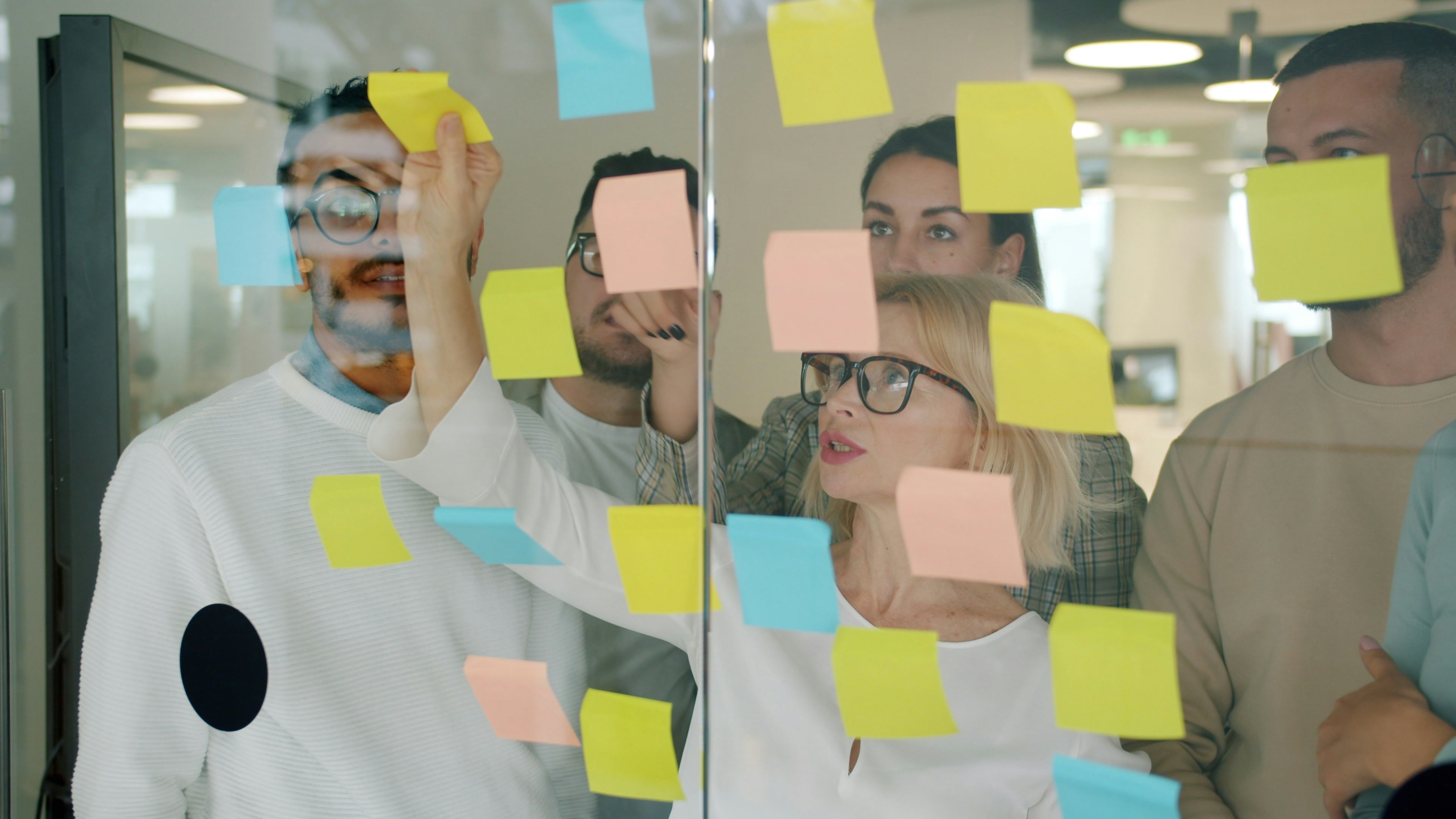 Close up shot of a diverse team brainstorming on a glass wall with colorful sticky notes in a modern office