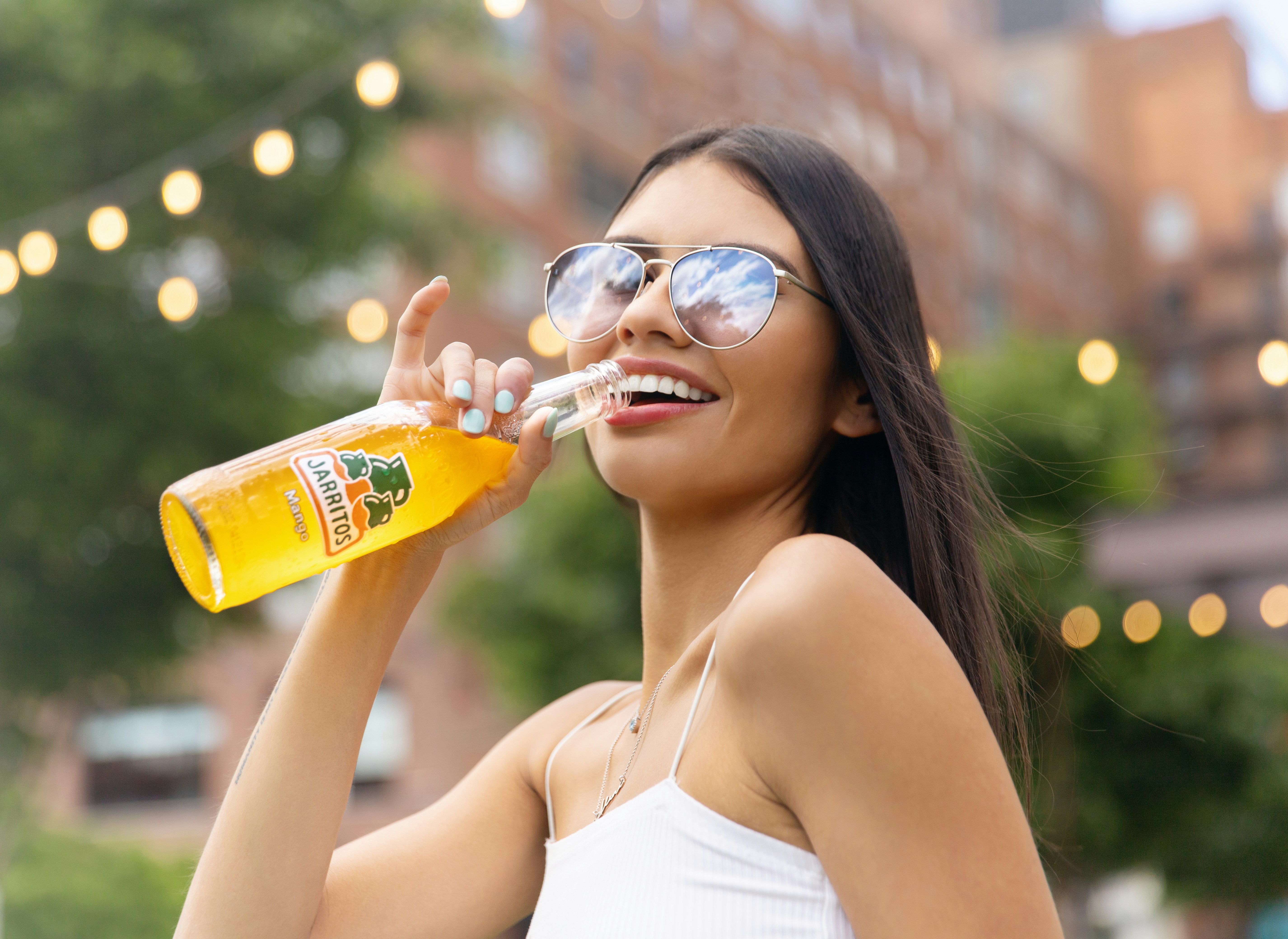 Close up photo of a smiling young woman drinking a sparkling mate drink in a glass bottle outside in the sun