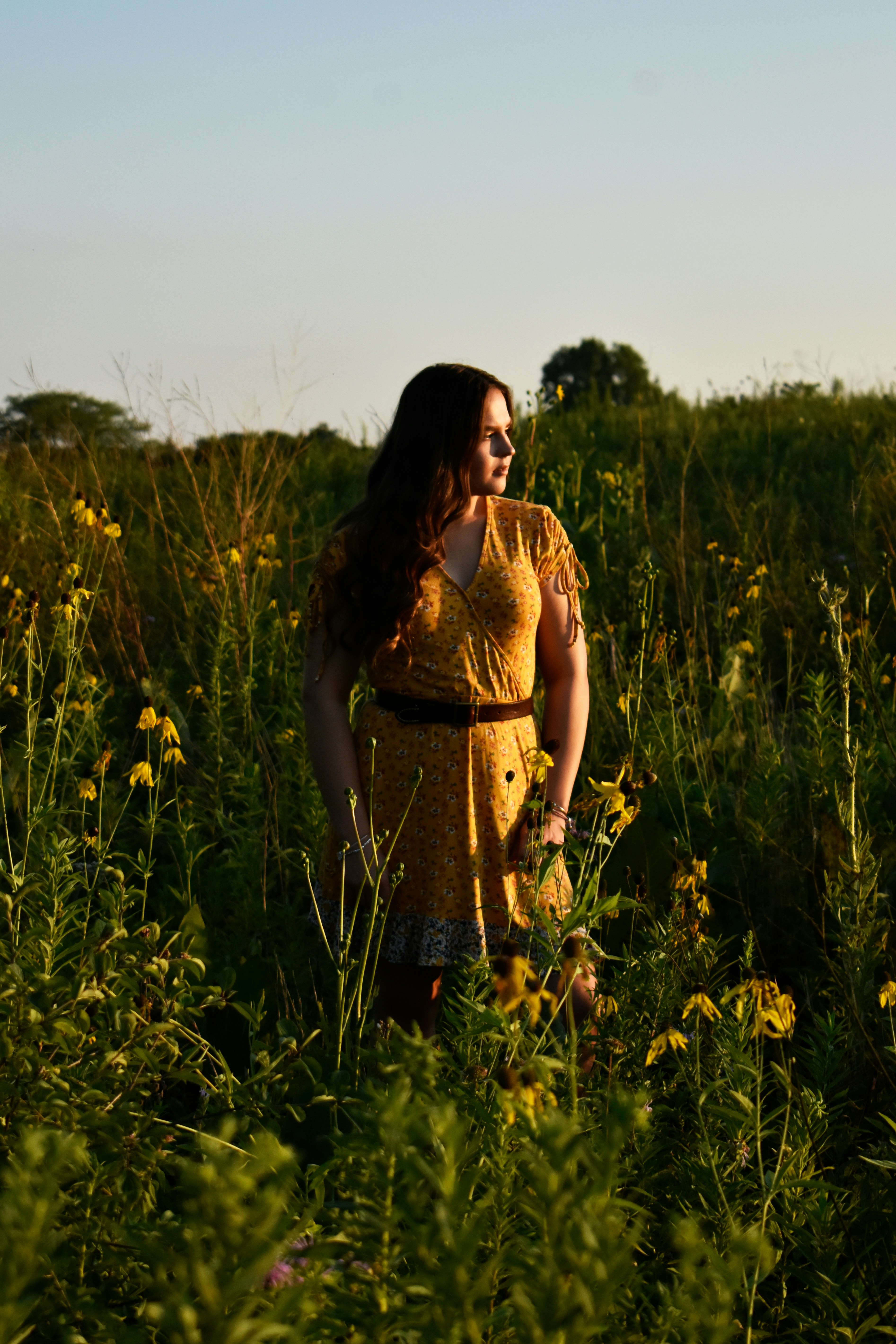 Woman wearing a long floral prairie dress in a field looking at sunset
