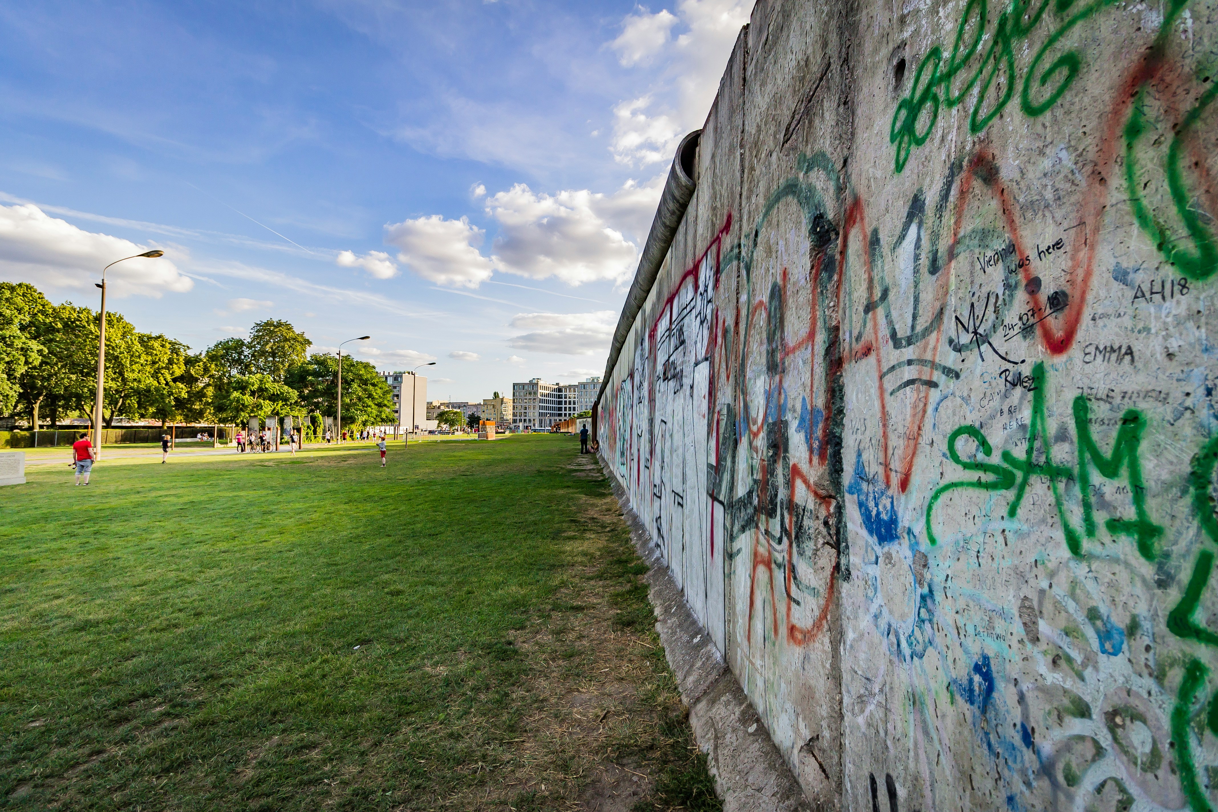 A colorful graffitied segment of the Berlin Wall displayed in a public park setting.