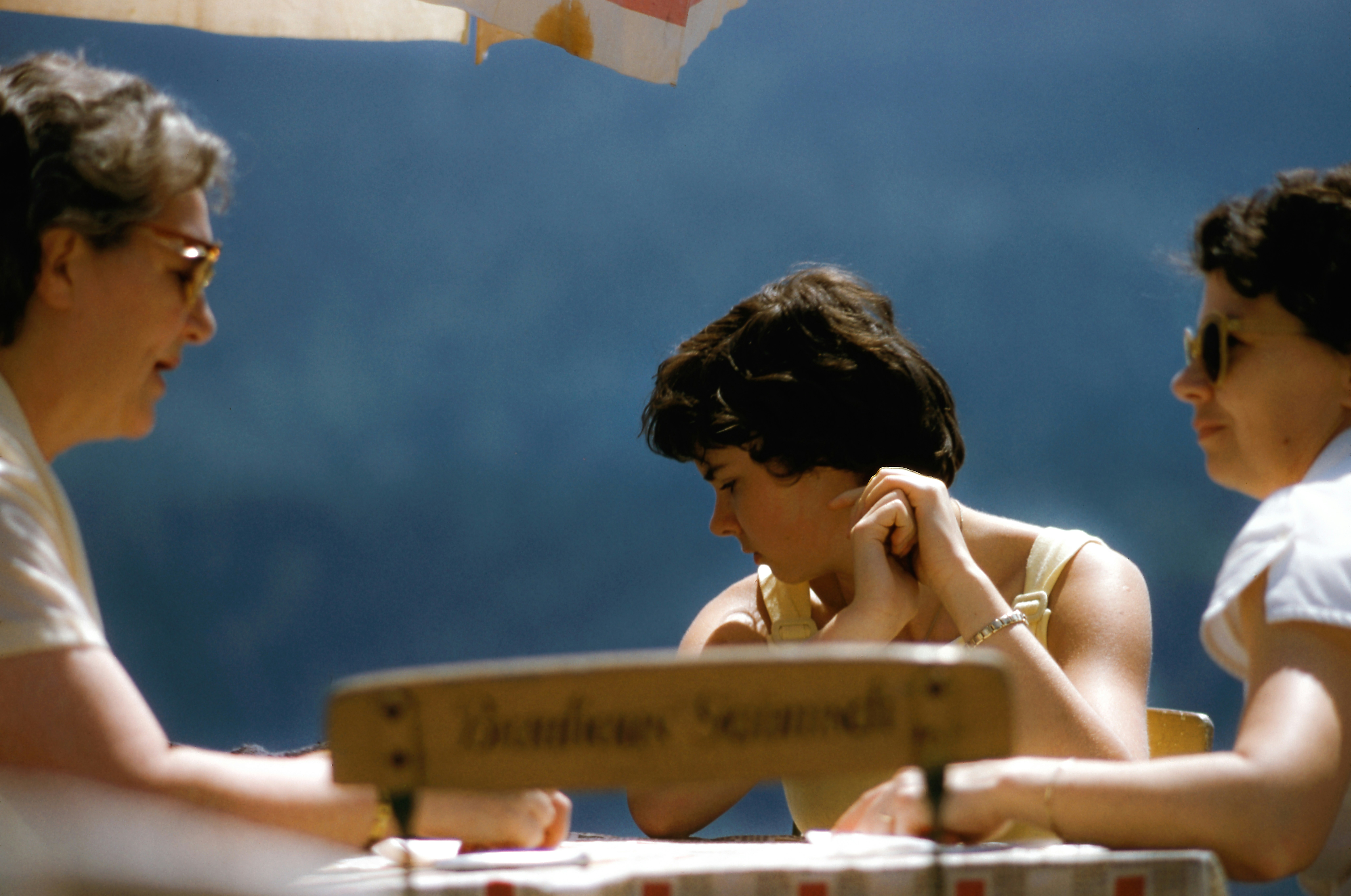Two people analyzing a document on a wooden desk, focus on the pen and paper with a calculator nearby