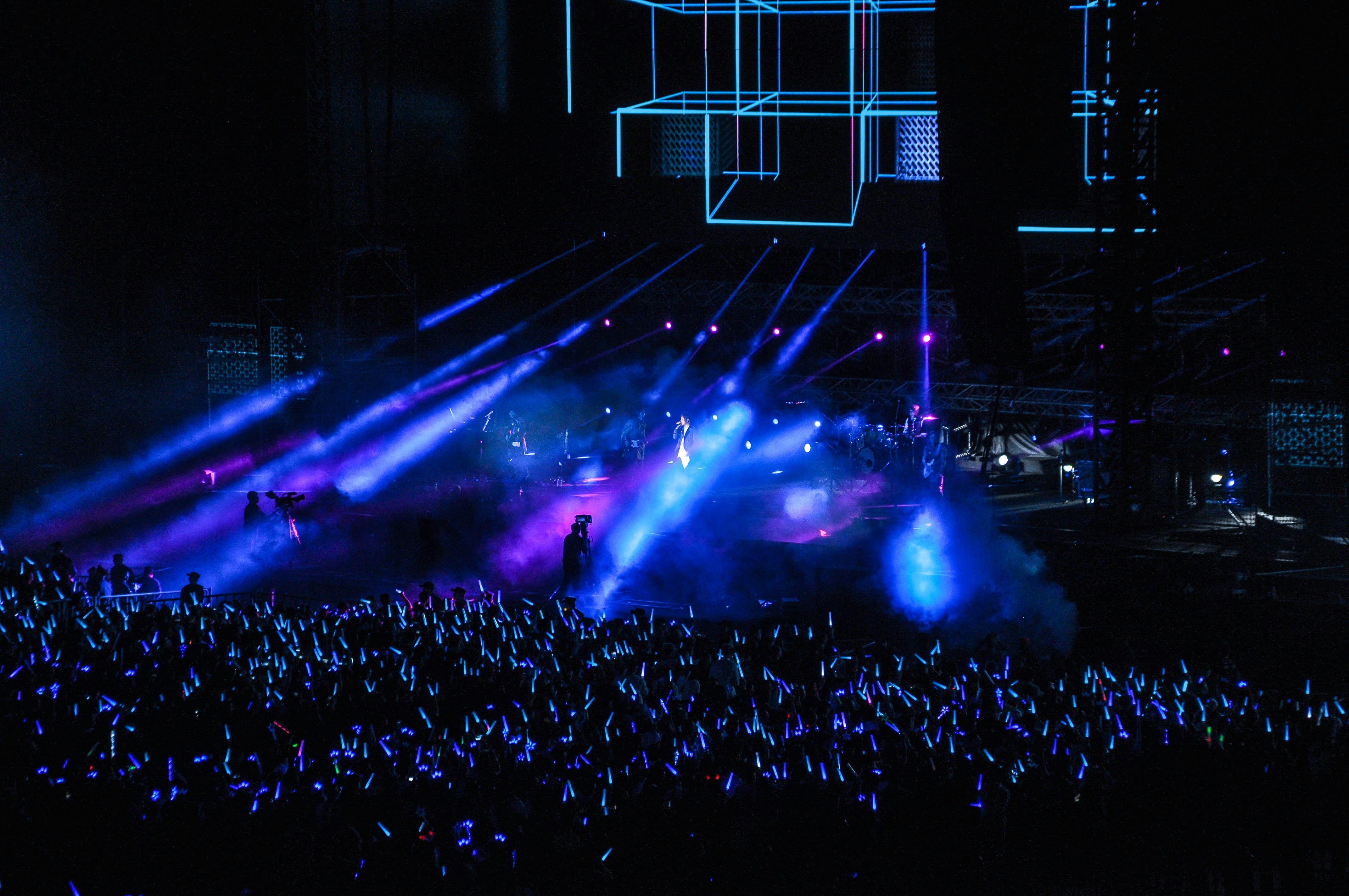 Concert crowd with hands raised, energetic atmosphere, blurred lights