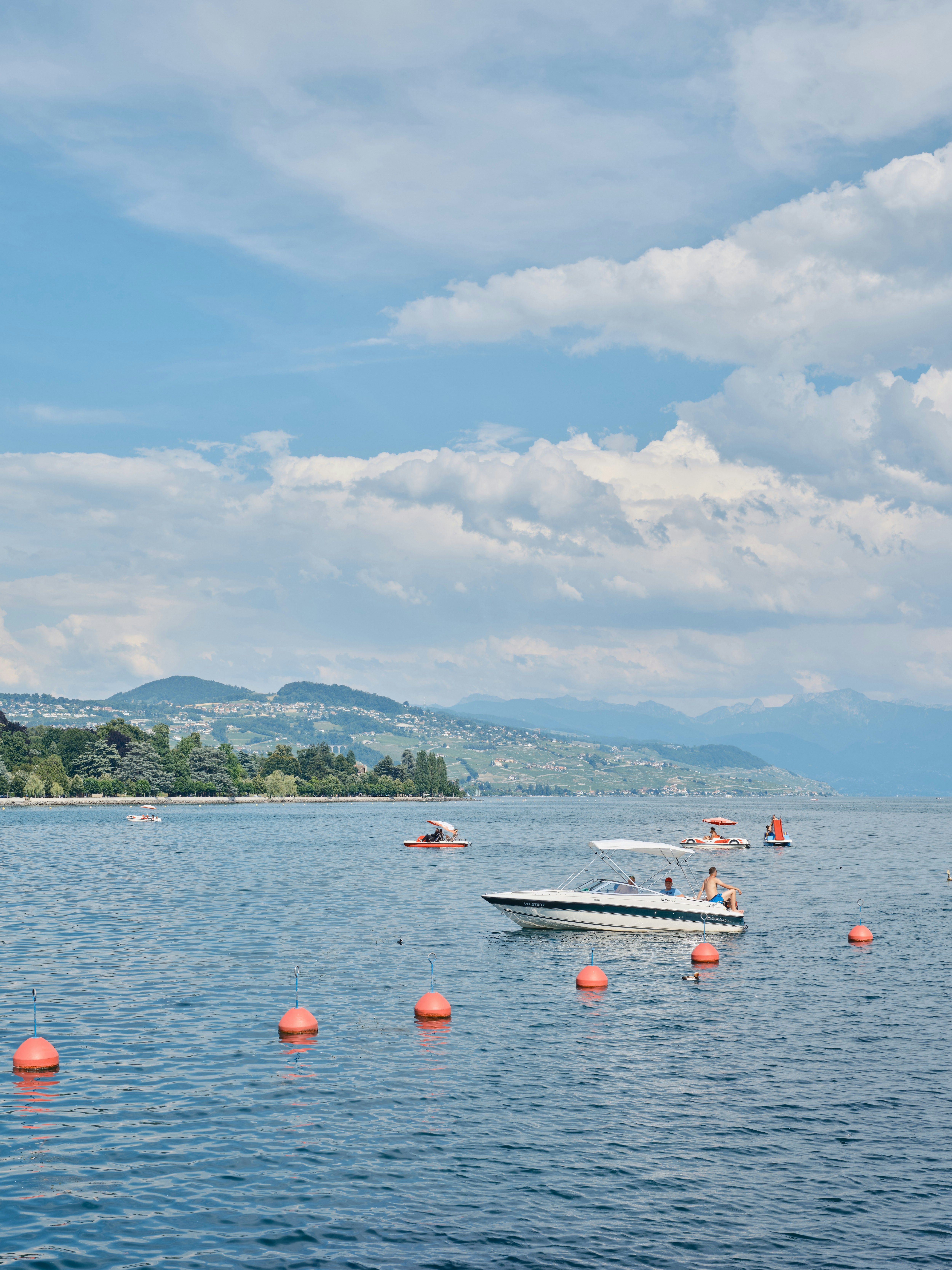 Wide shot of a couple on a boat in the middle of Lake Geneva with mountains in the background.