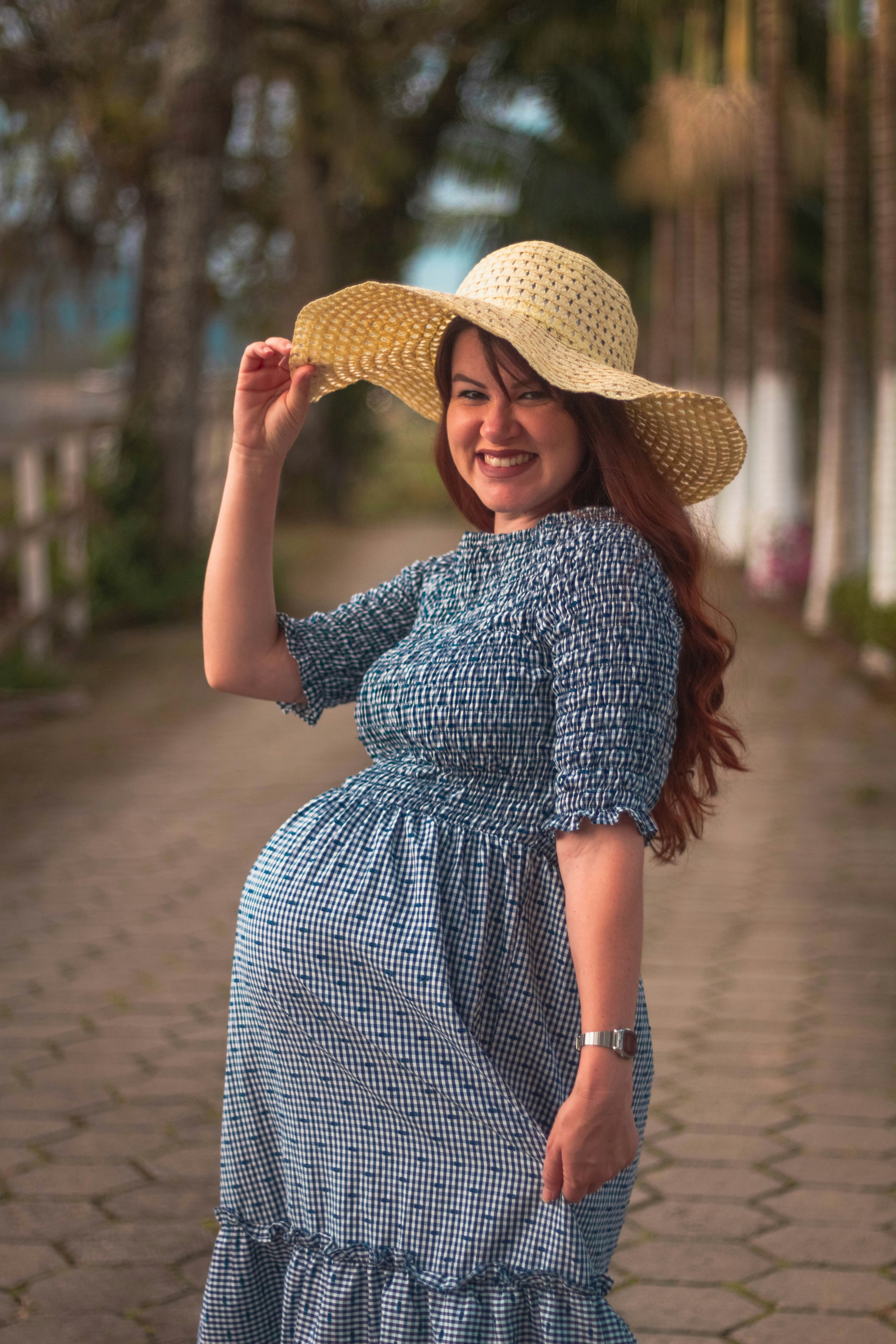 A happy pregnant woman showing a baby outfit to the camera in a natural outdoor setting