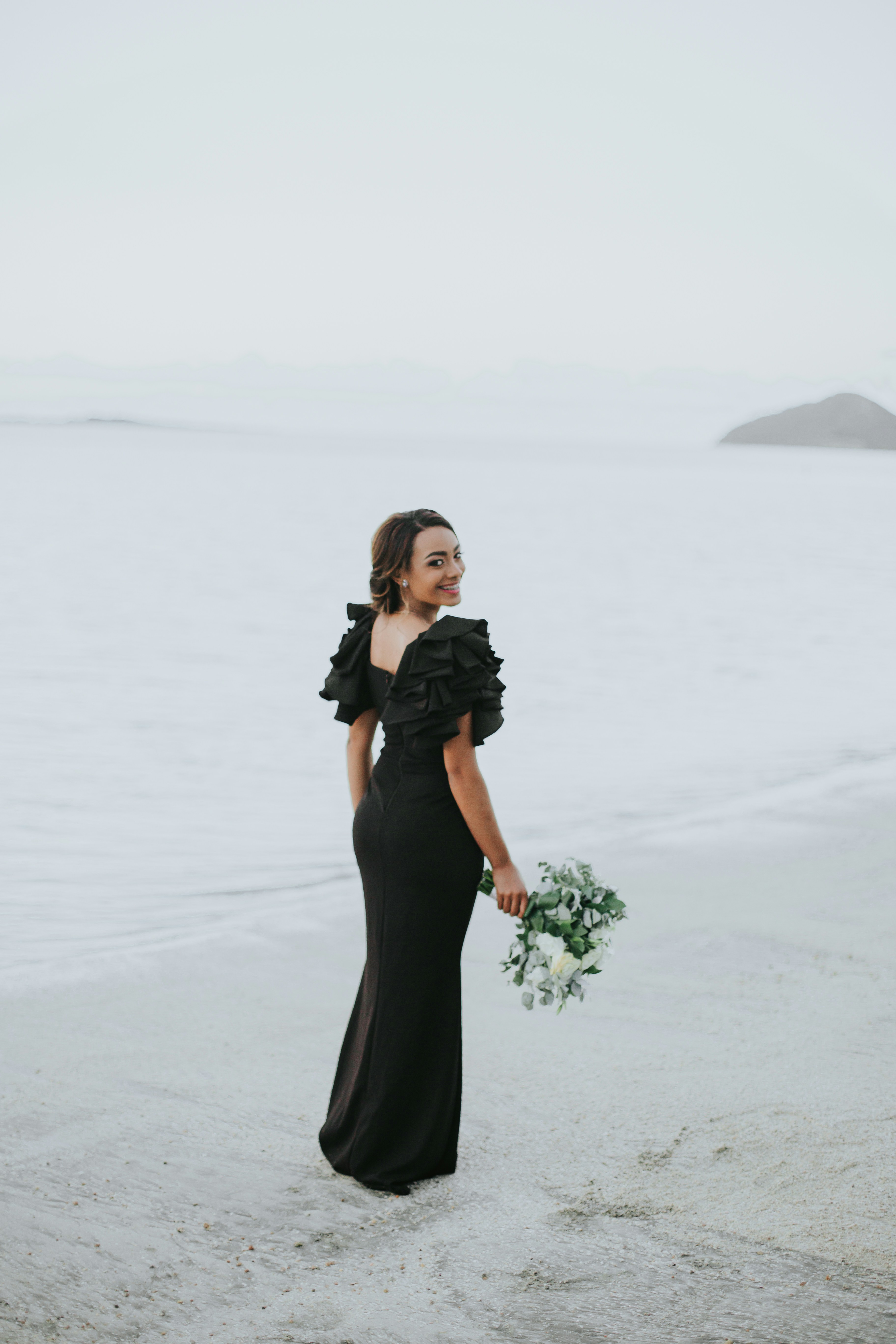 Woman wearing a elegant black floral slip dress standing near a modern beach house vibe