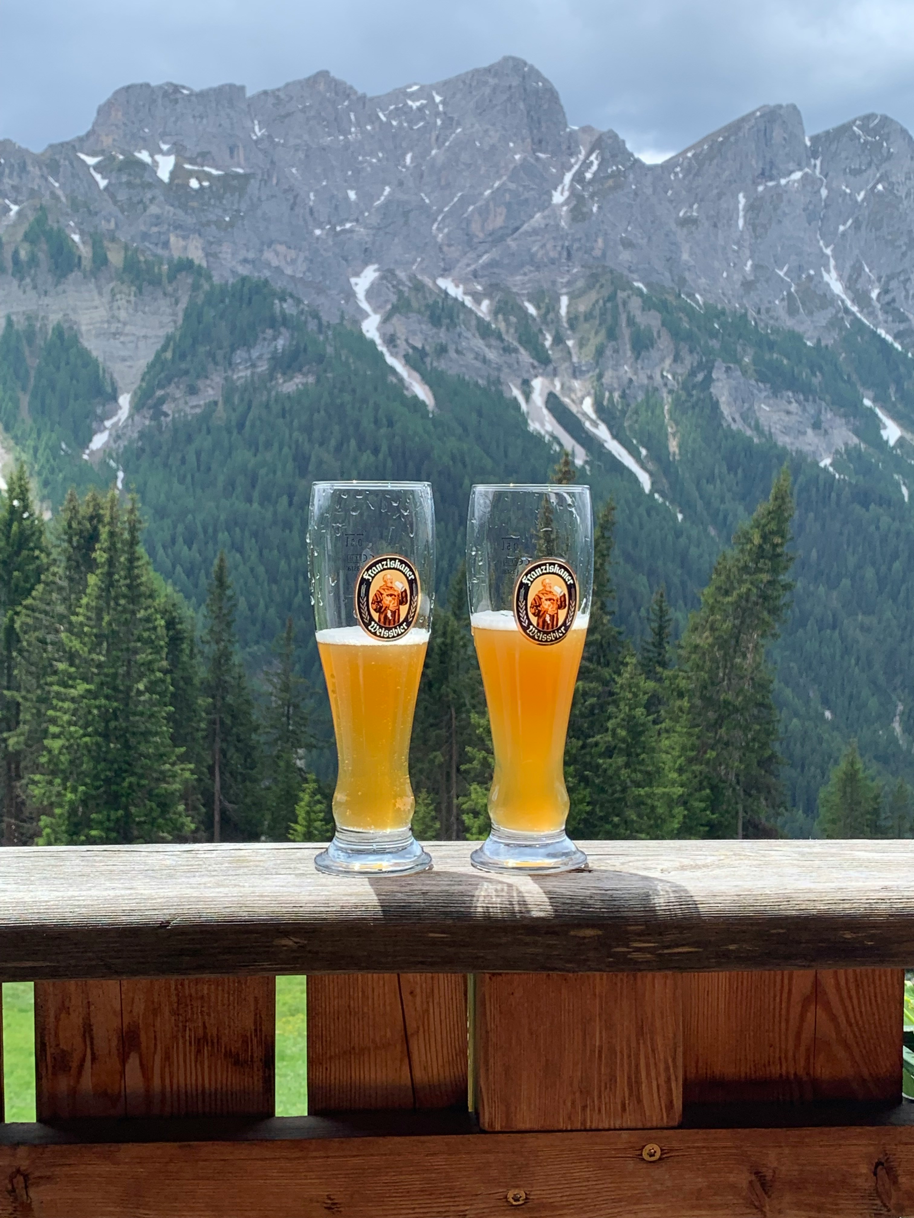 Wide shot of a wooden bar counter at a Swiss summer festival with draft beer towers serving mate, mountains in background.